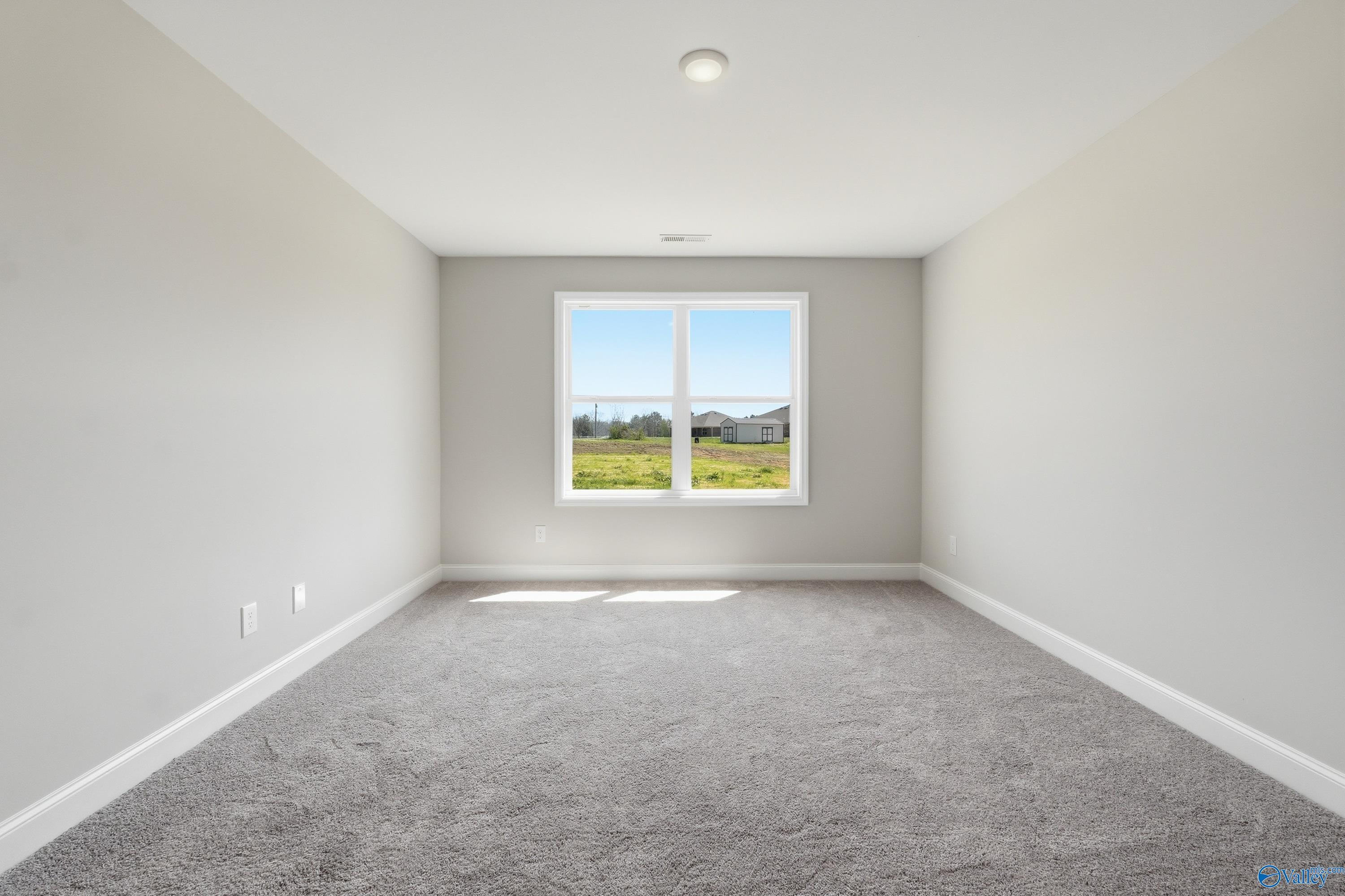 Bright empty bedroom with large sunny window and carpeted floors in Davidson Homes The Franklin V, Athens, Alabama
