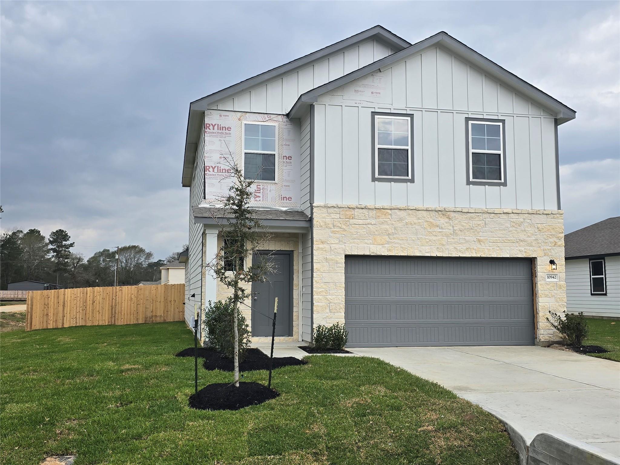 Two-story 5-bedroom Davidson Homes Brazos E with white siding, stone accents, gray 2-car garage, and landscaped yard in Liberty Estates, Cleveland, Texas