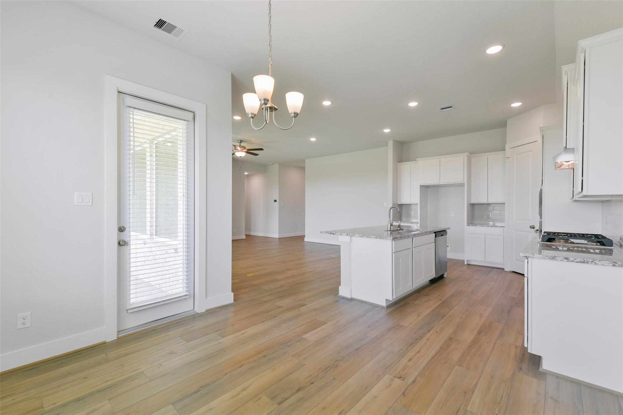 Open-concept kitchen with white island sink, dishwasher, hardwood floors in Davidson Homes The Edward A, Lago Mar, Texas City