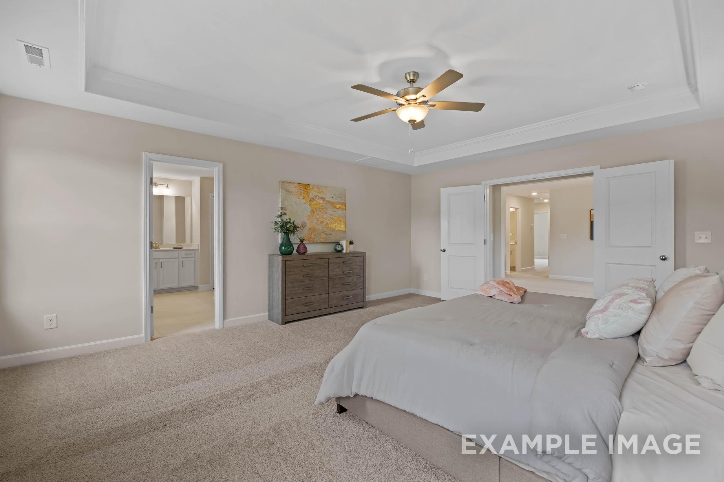 Spacious master bedroom in The Preston B with king bed, beige walls, ceiling fan, and en-suite bath access by Davidson Homes