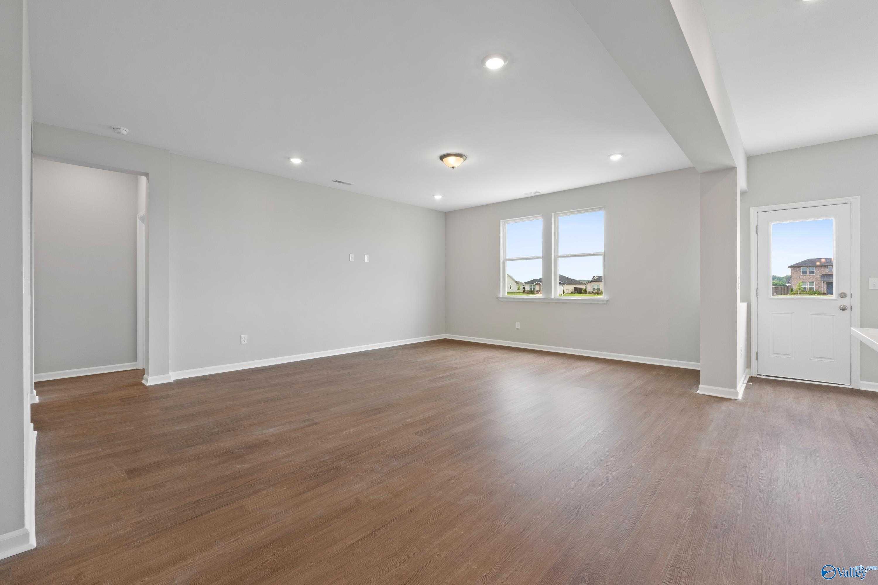 Spacious empty great room with hardwood floors, gray walls, large windows in Davidson Homes The Dorado, Athens Alabama