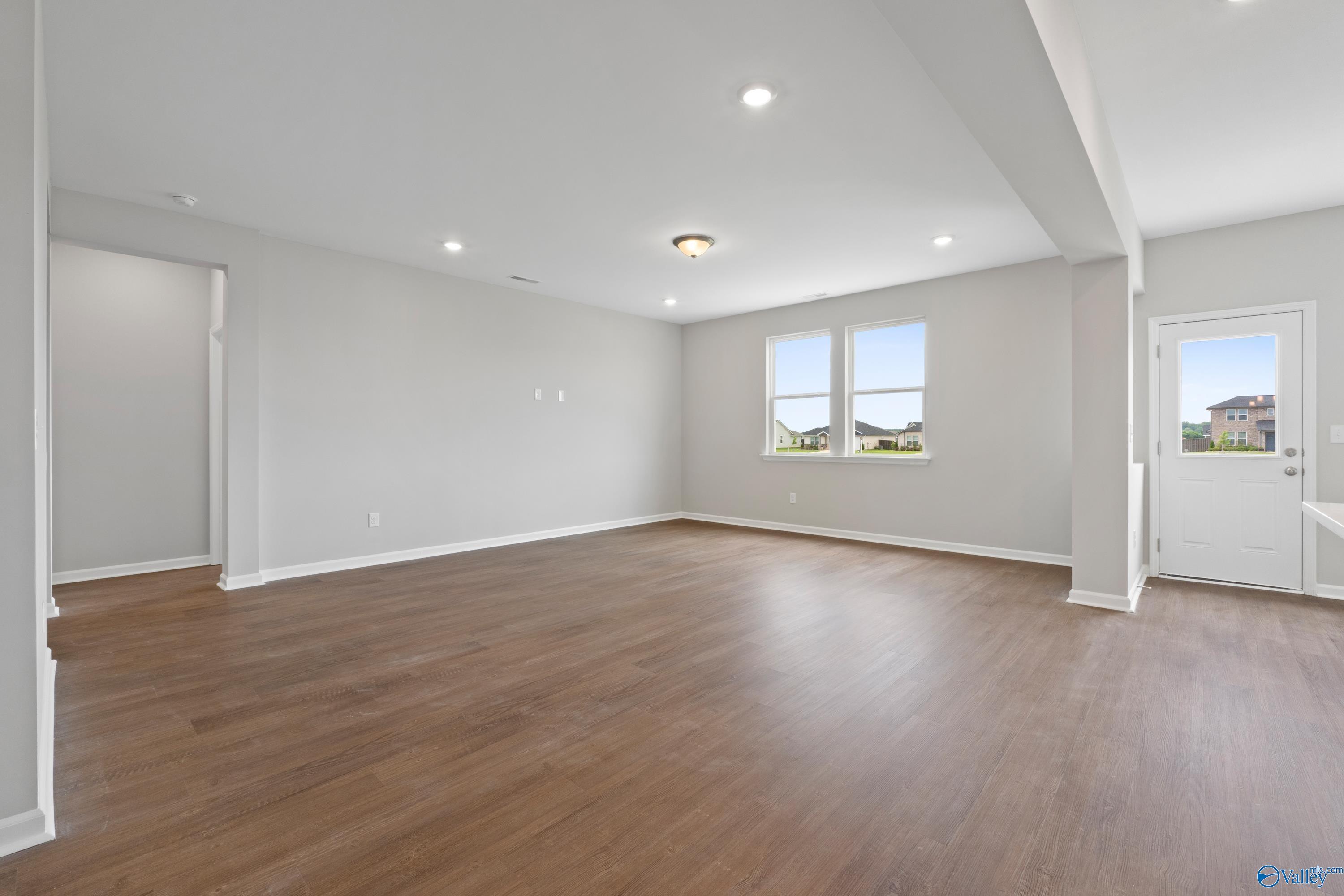 Spacious empty living room with gray walls, hardwood floors, large windows, and French doors in Davidson Homes The Dorado, Athens AL