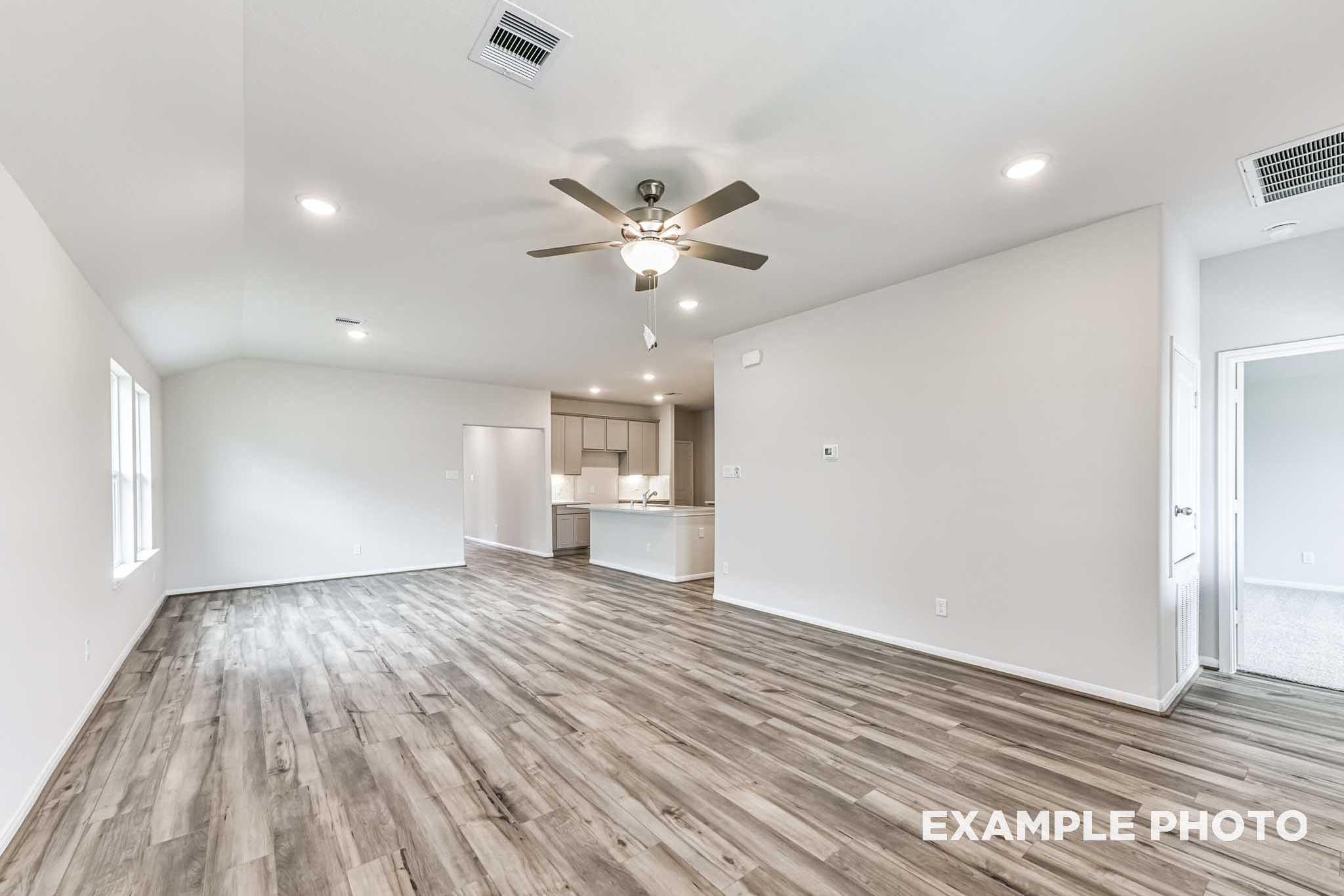 Spacious open-concept living and kitchen in The Laguna A with gray wood flooring, white cabinets, ceiling fan, and recessed lights