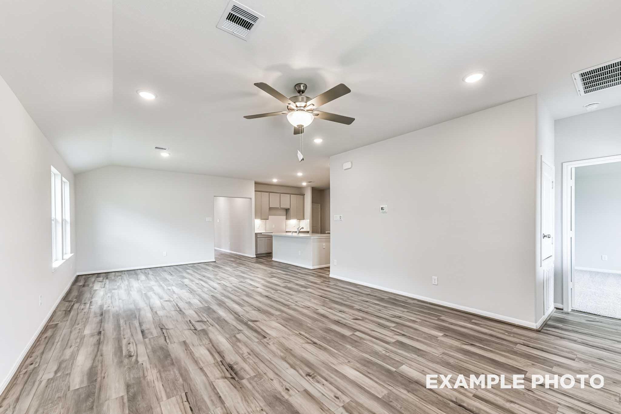 Spacious open-concept living and kitchen in The Laguna A with gray wood flooring, white cabinets, ceiling fan, and recessed lights