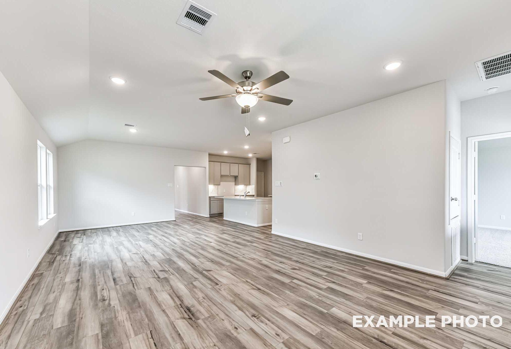 Spacious open-concept living and kitchen in The Laguna A with gray wood flooring, white cabinets, ceiling fan, and recessed lights