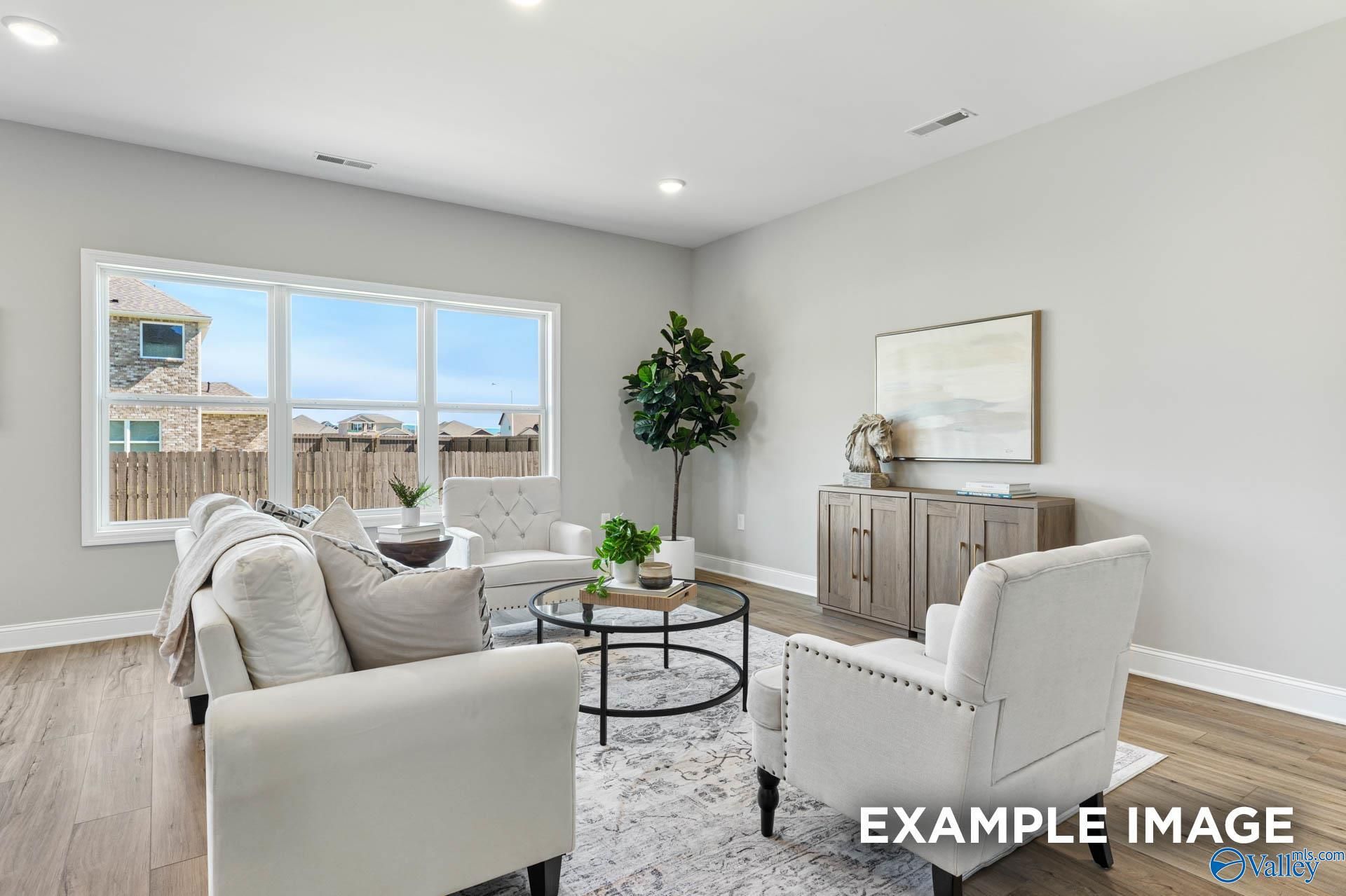 Bright living room with white sofa, armchairs, plants, and large windows in Davidson Homes Chelsea B, Toney AL