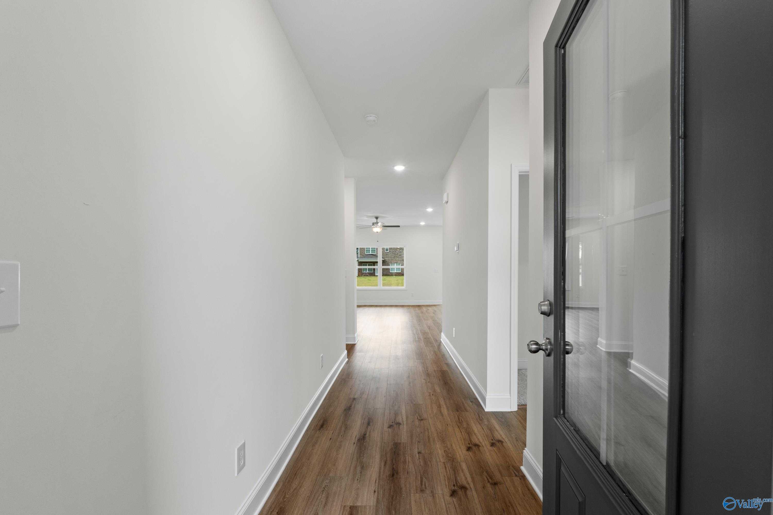 Bright hallway with hardwood floors, white walls, and glass door to backyard in Davidson Homes The Asheville C, Athens, Alabama