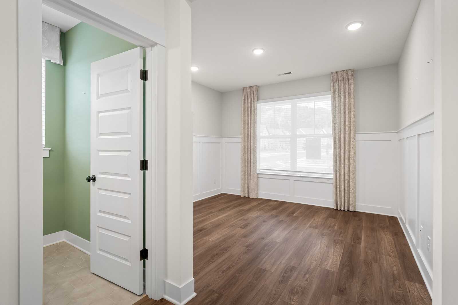 Elegant bedroom with white wainscoting, hardwood floors, and large curtained window in Davidson Homes The Ridgeport, Gallatin TN