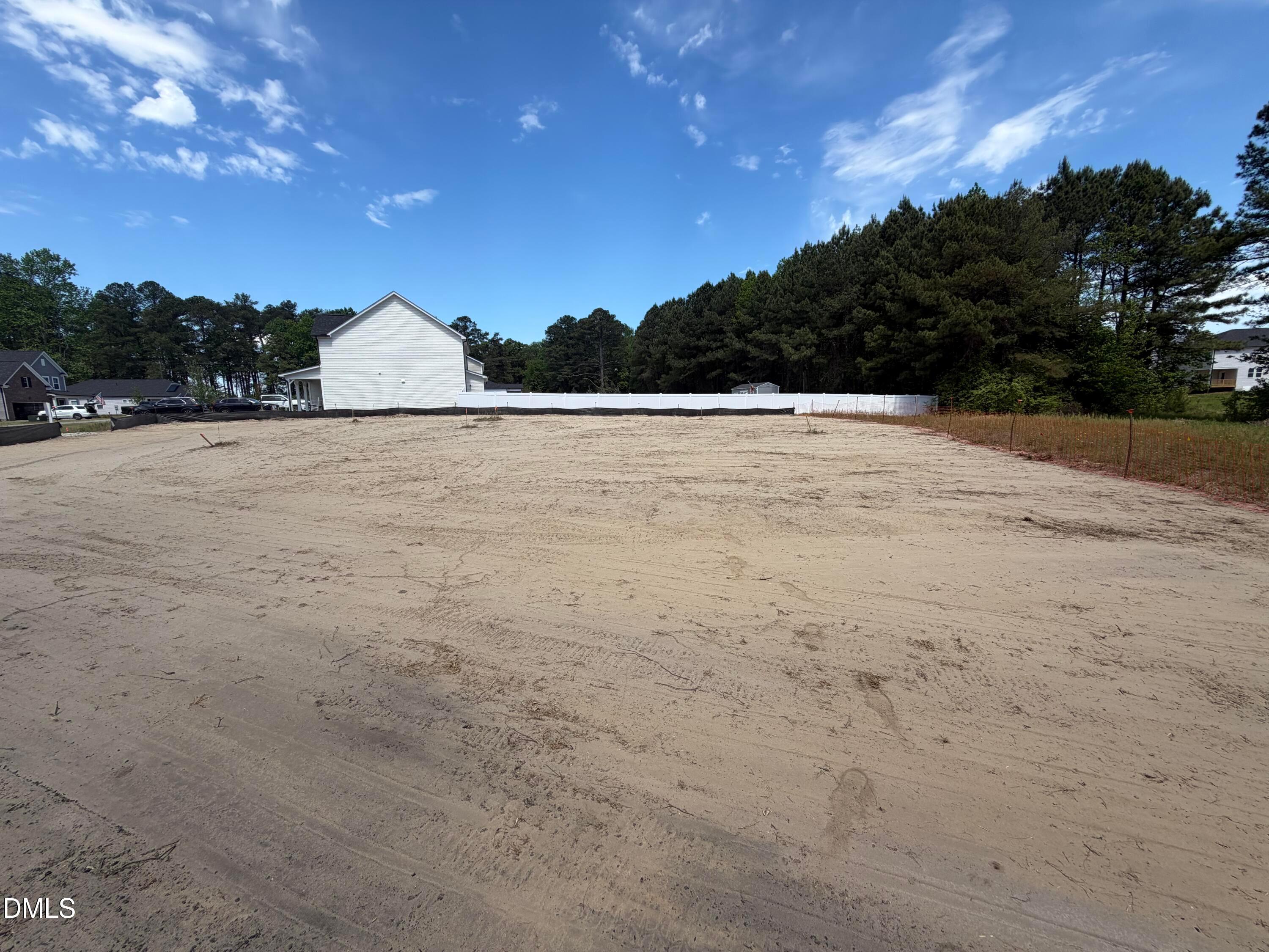 Cleared sandy lot with white privacy fence, pine trees, and nearby homes in Wellers Knoll, Lillington, for Davidson Homes Willow D