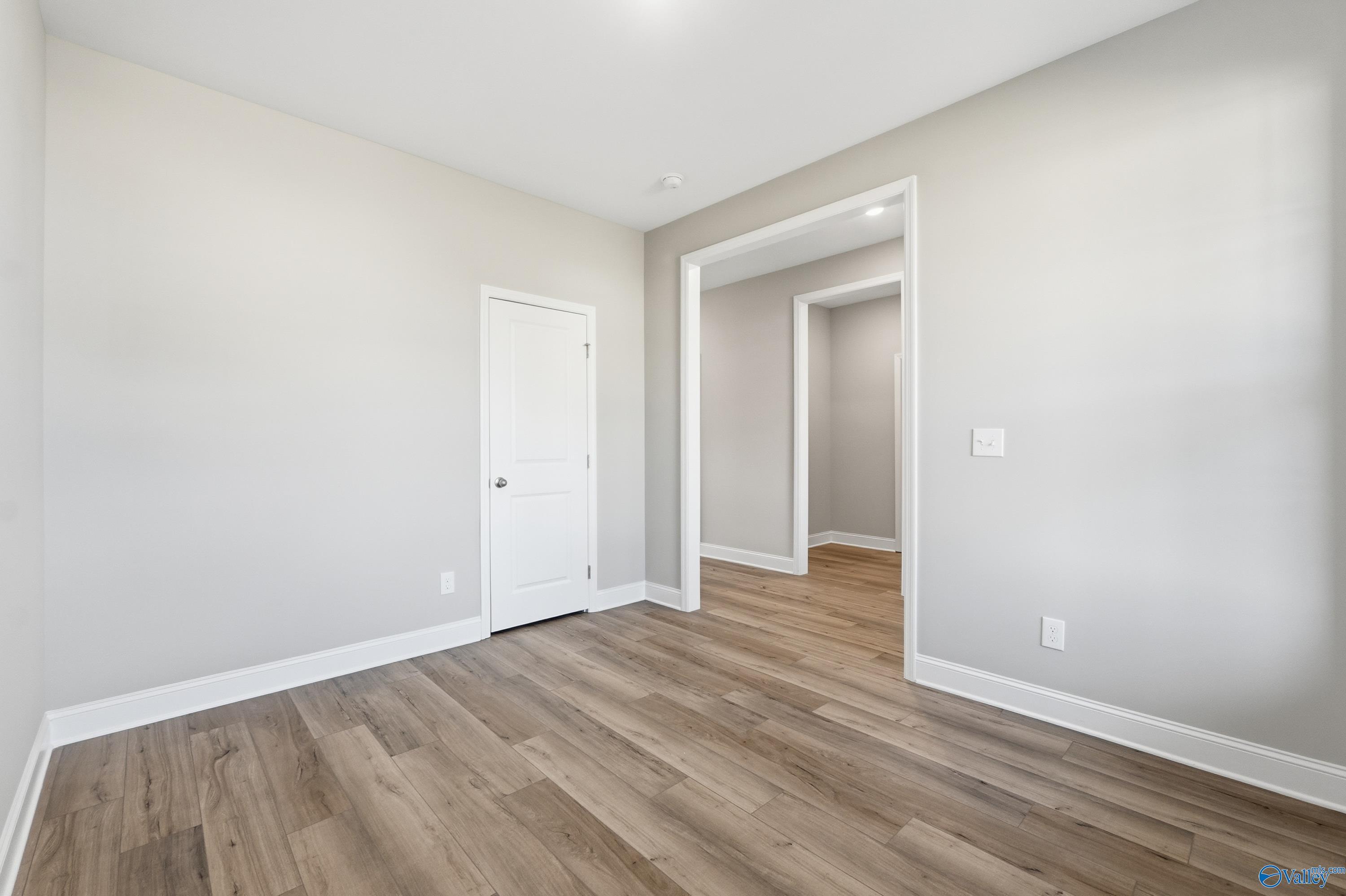 Bright secondary bedroom with neutral walls, white door, and luxury vinyl plank flooring in Davidson Homes The Rockford, Harvest AL