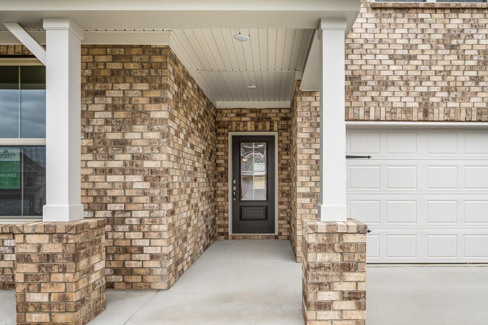 Brick home facade with covered front porch, white columns, dark door, and 2-car garage in Davidson Homes The Ridgeport C, Gallatin, TN