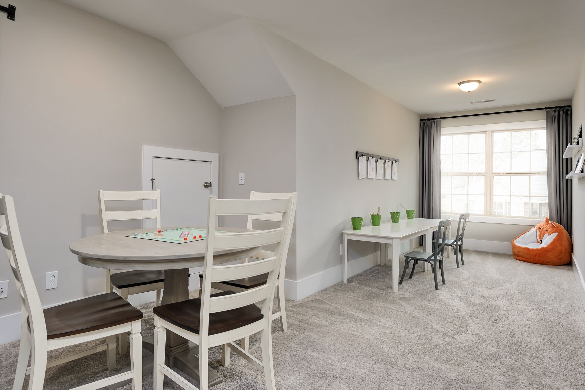 Cozy playroom in Chimney Creek Hampton Cove AL home with sloped ceiling, game table, white chairs, orange bean bag, and window nook