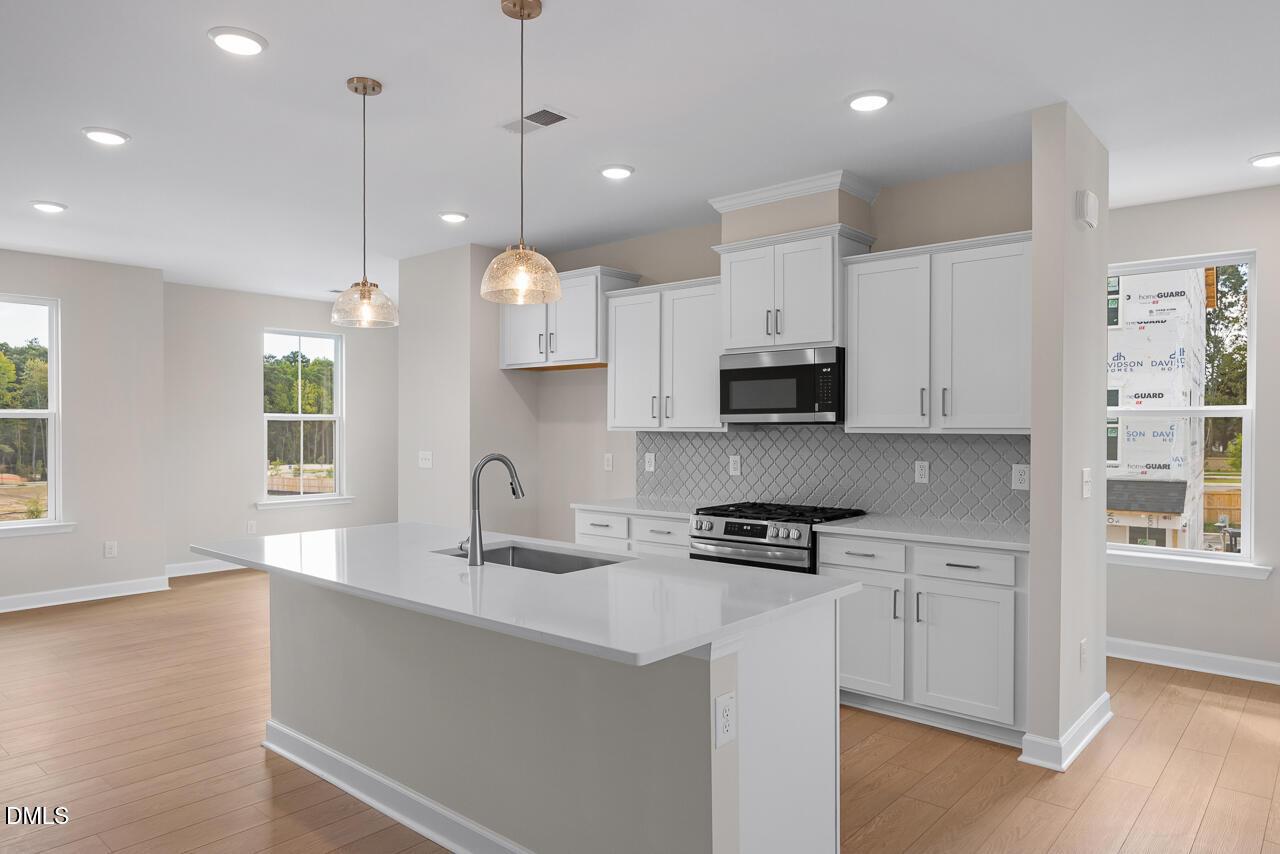 Bright open-concept kitchen with white cabinetry, island, and pendant lights in The Mitchell floor plan, Knightdale, NC by Davidson Homes