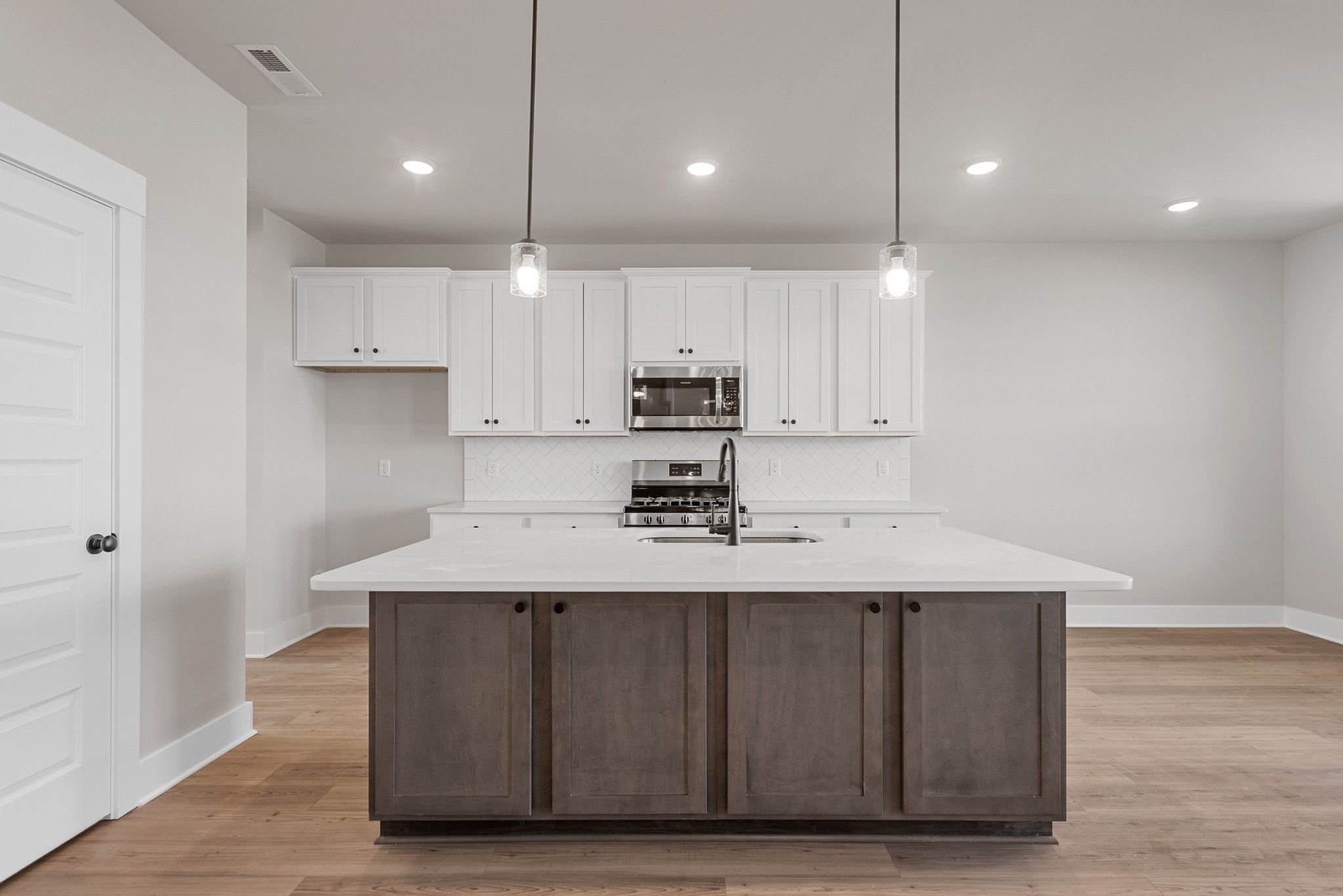 Modern kitchen with white cabinets, large dark wood island, and stainless appliances in The Willow B, Calista Farms home.