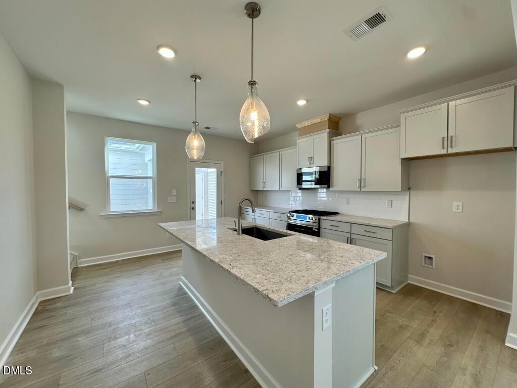 Modern kitchen featuring granite island sink, stainless appliances, and pendant lights in Davidson Homes The Burke, Knightdale, NC