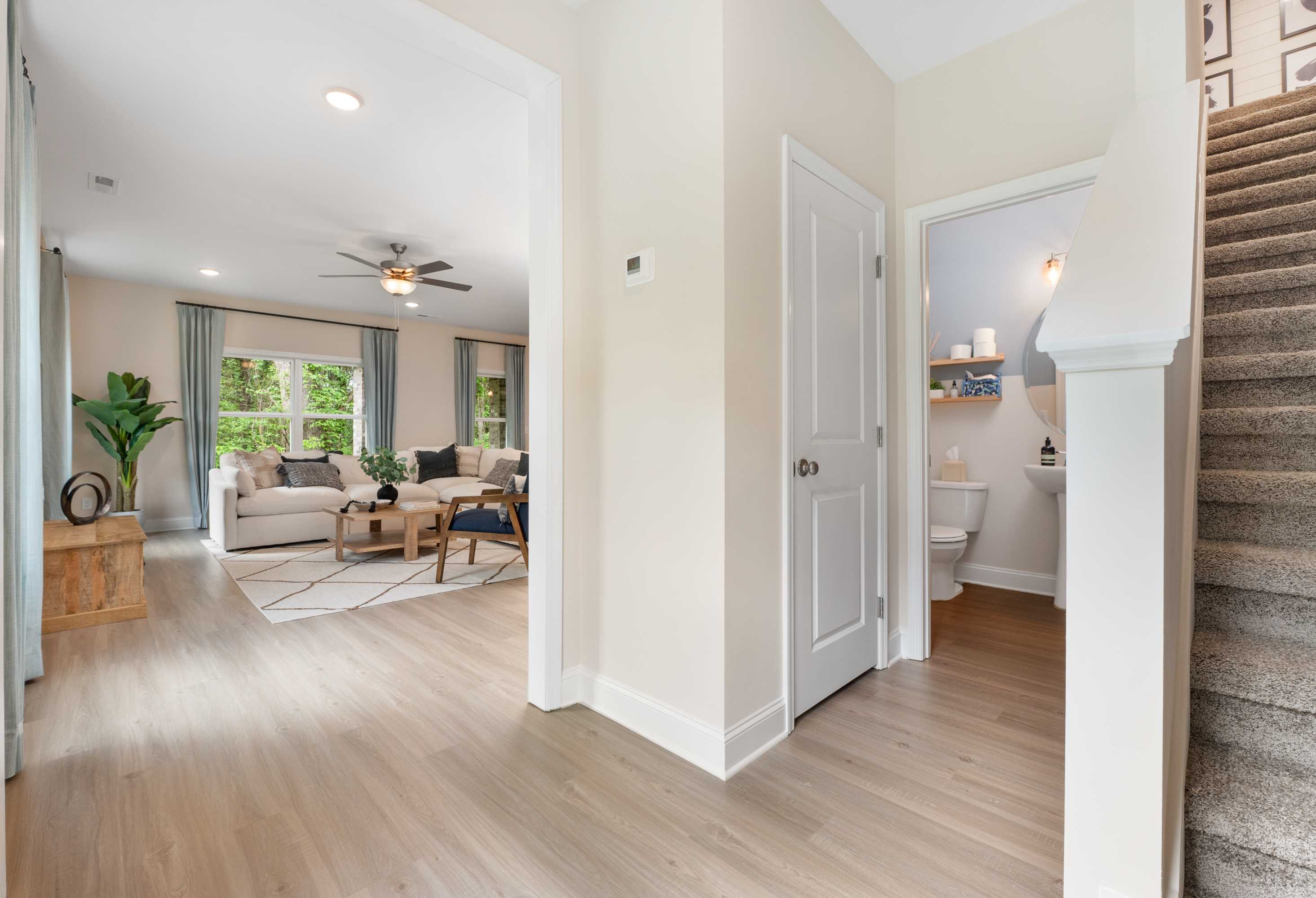 Spacious foyer of The Camden showcasing open staircase, living area with sofa and ceiling fan, powder room