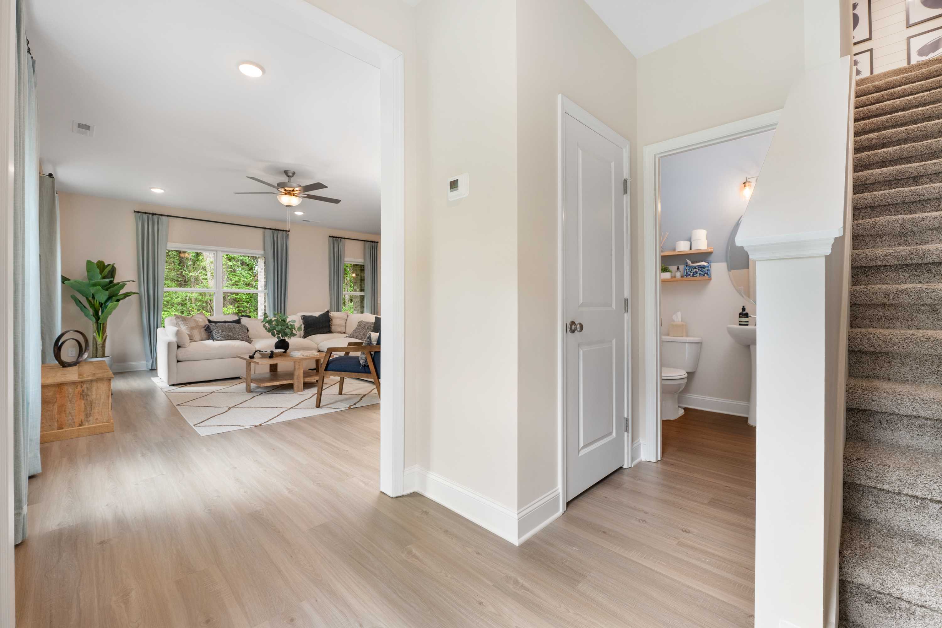 Open-concept foyer in Pavilion Huntsville AL home with light oak floors, beige walls, living area seating, powder room, and staircase