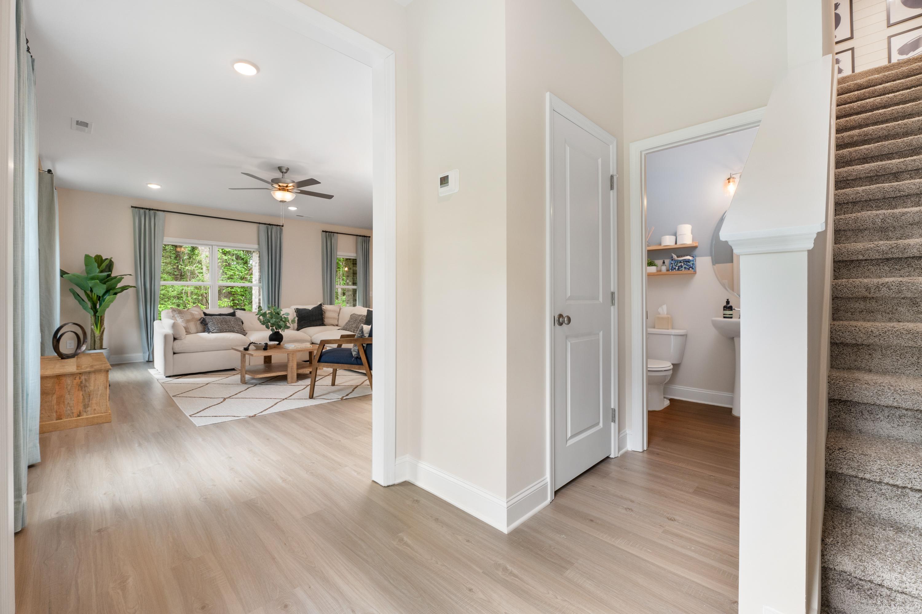 Open-concept foyer in Pavilion Huntsville AL home with light oak floors, beige walls, living area seating, powder room, and staircase