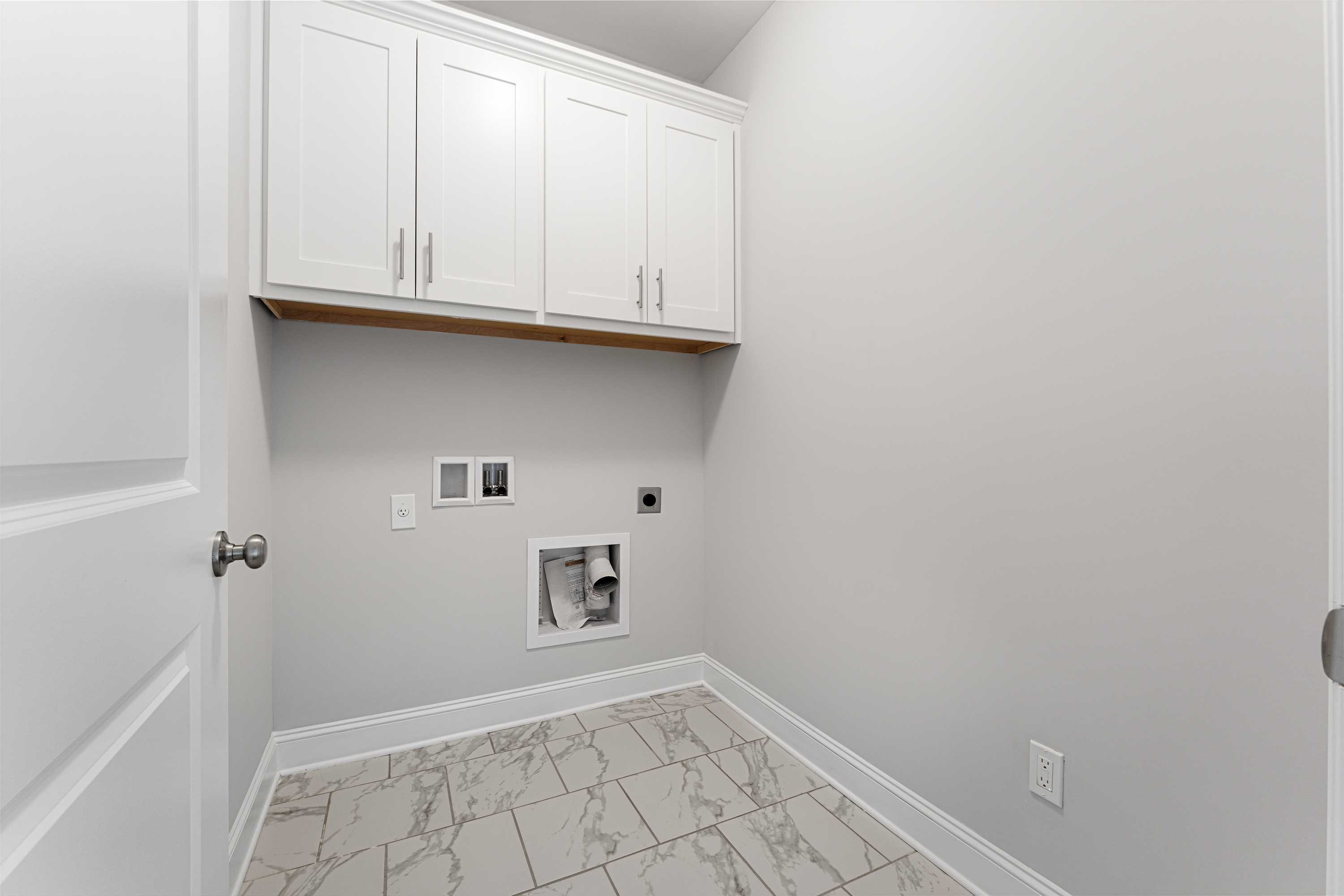 Modern laundry room in The Copeland B featuring white upper cabinets, gray walls, utility hookups, and porcelain tile floor