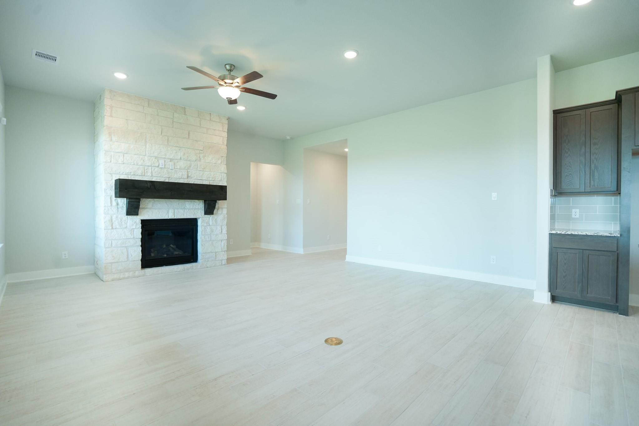 Spacious living room with stone fireplace, wood mantel, ceiling fan, and light floors in Davidson Homes The Edward C, Lago Mar, Texas City