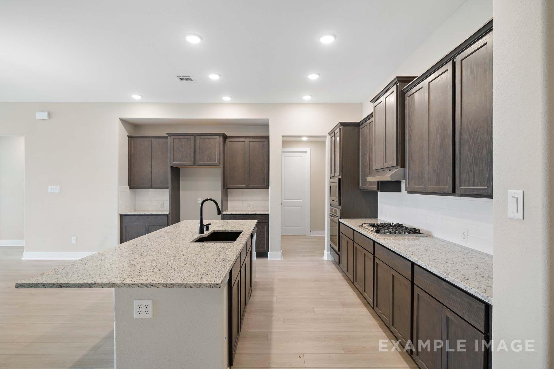 Gourmet kitchen in The Elizabeth by Davidson Homes featuring granite island, dark cabinets, and gas cooktop in Texas City.