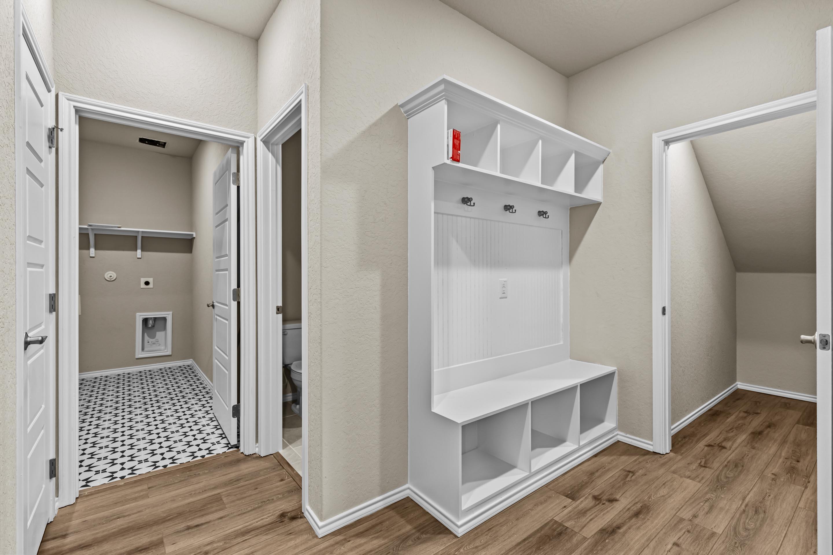 White mudroom cabinetry with bench, hooks, and cubbies next to laundry room in Davidson Homes The Douglas F, Royal Crest, San Antonio