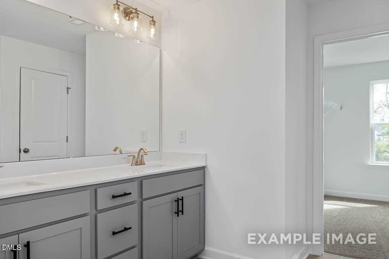 Modern double vanity with gray shaker cabinets, gold faucet, and large mirror in master bath of The Willow D home, Zebulon, NC