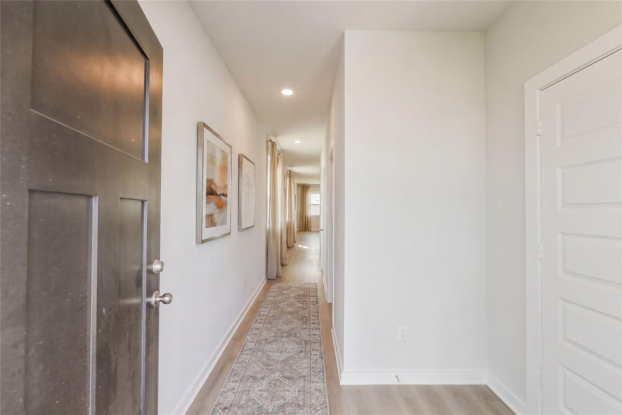 Bright entry hallway with modern dark door, abstract wall art, patterned runner rug on oak floors in The Frio G, Conroe Texas