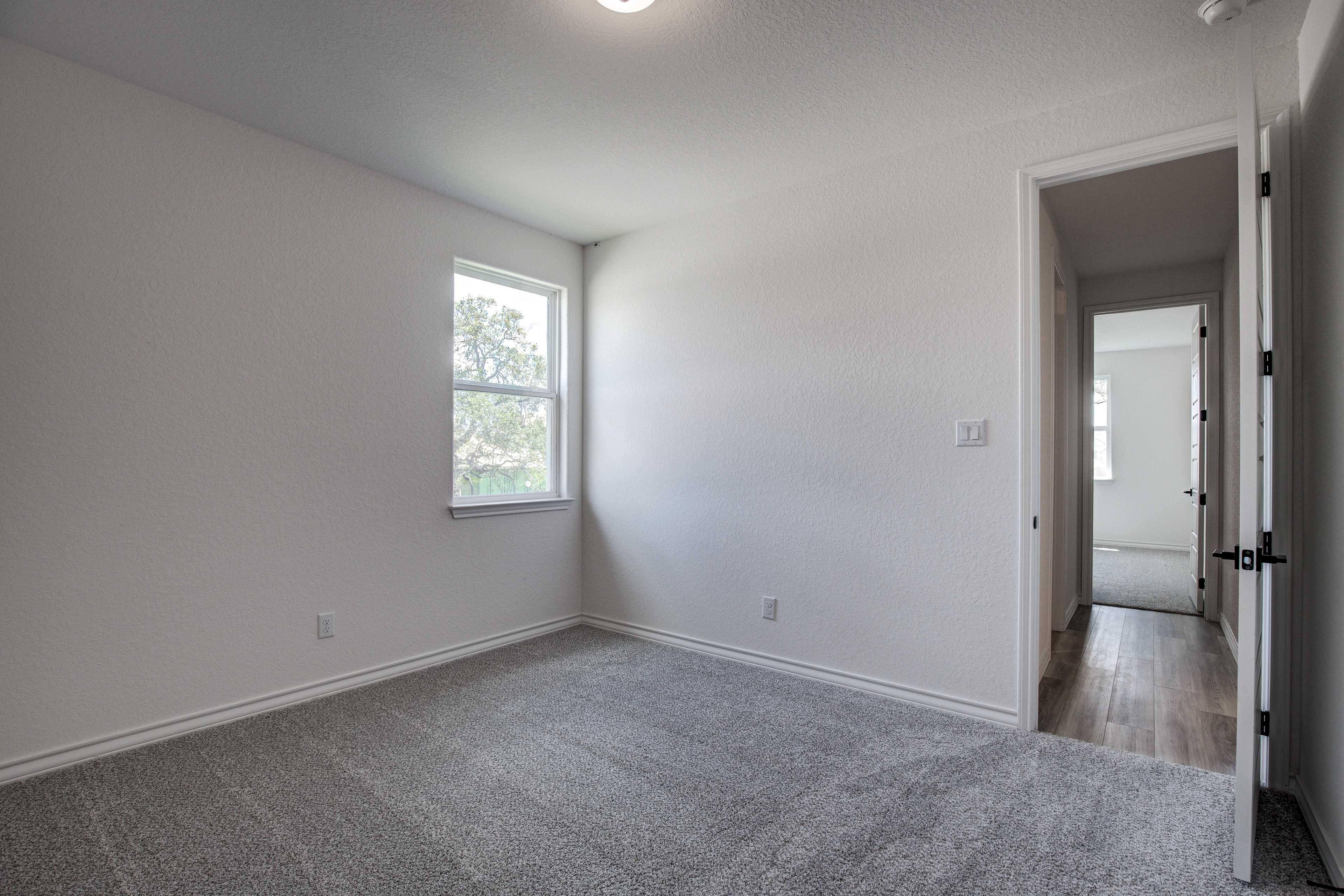 Spacious secondary bedroom in The Lanier by Davidson Homes featuring gray carpet, large window with blinds, and open doorway