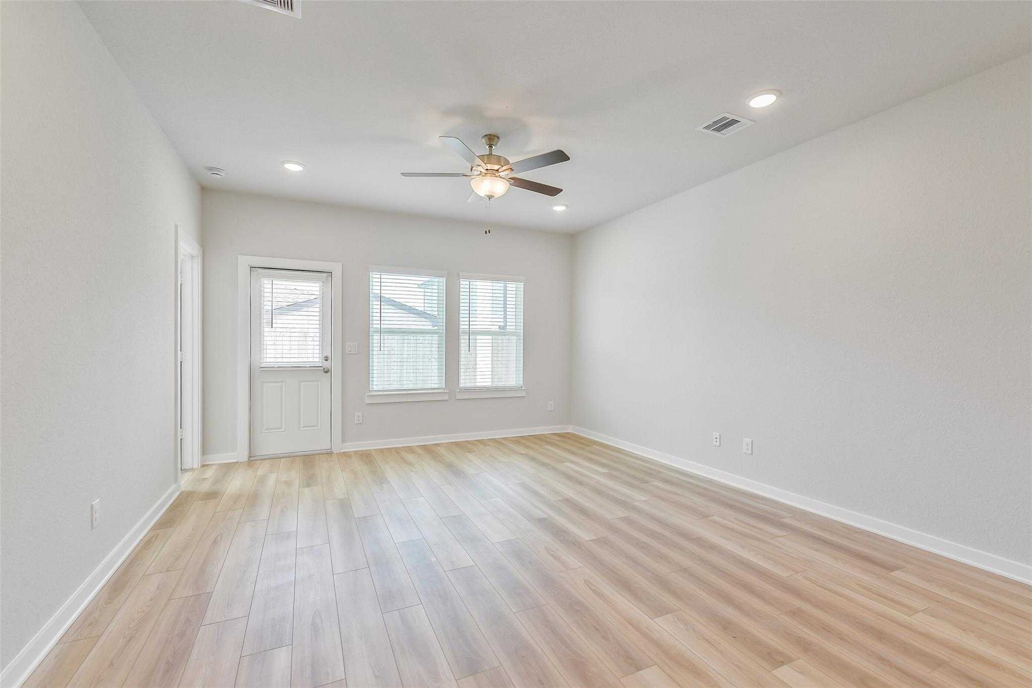 Spacious empty living room with light hardwood floors, ceiling fan, and large windows in 5-bedroom Davidson Homes The Rio Grande H, Magnolia, Texas