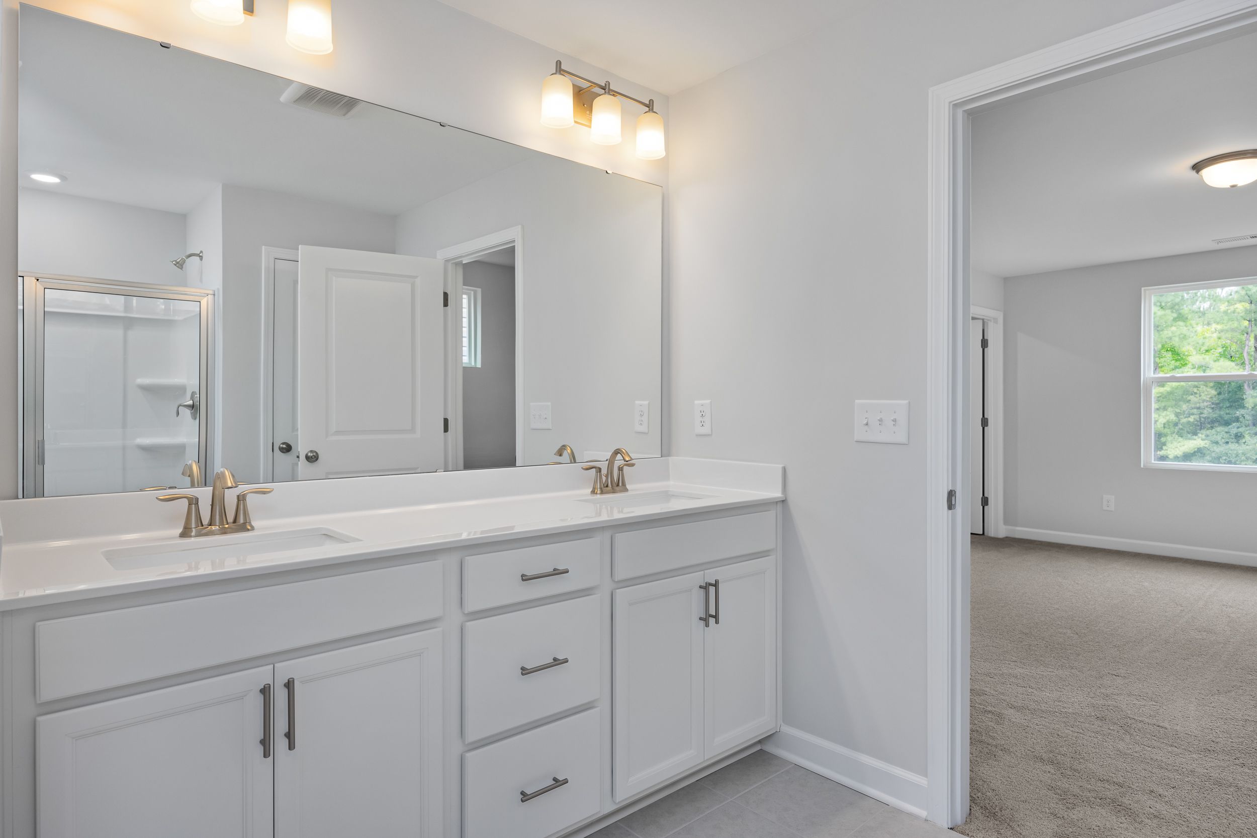 Modern master bathroom in The Durham featuring double vanity, white cabinetry, and a spacious walk-in shower.
