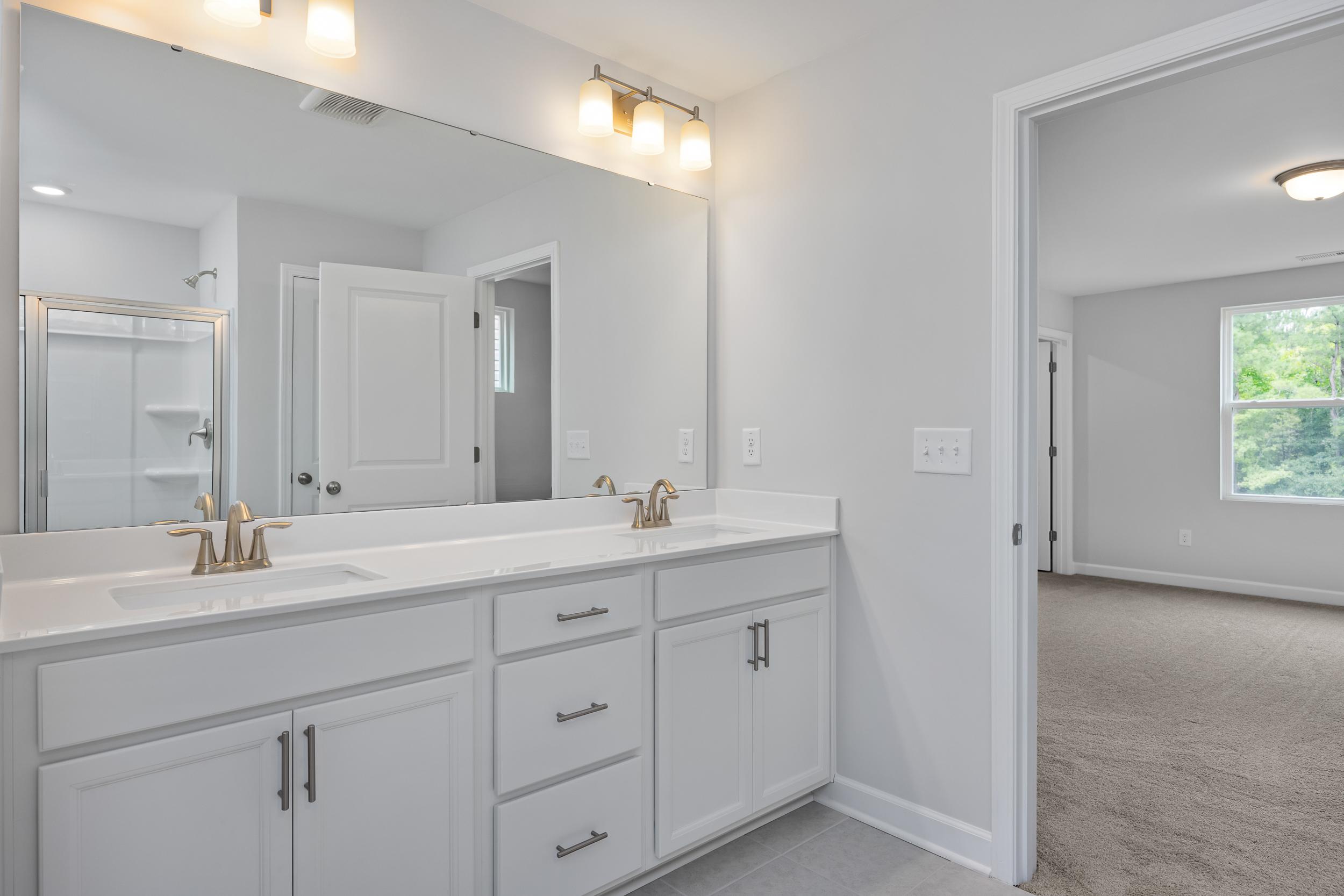 Modern master bathroom in The Durham featuring double vanity, white cabinetry, and a spacious walk-in shower.