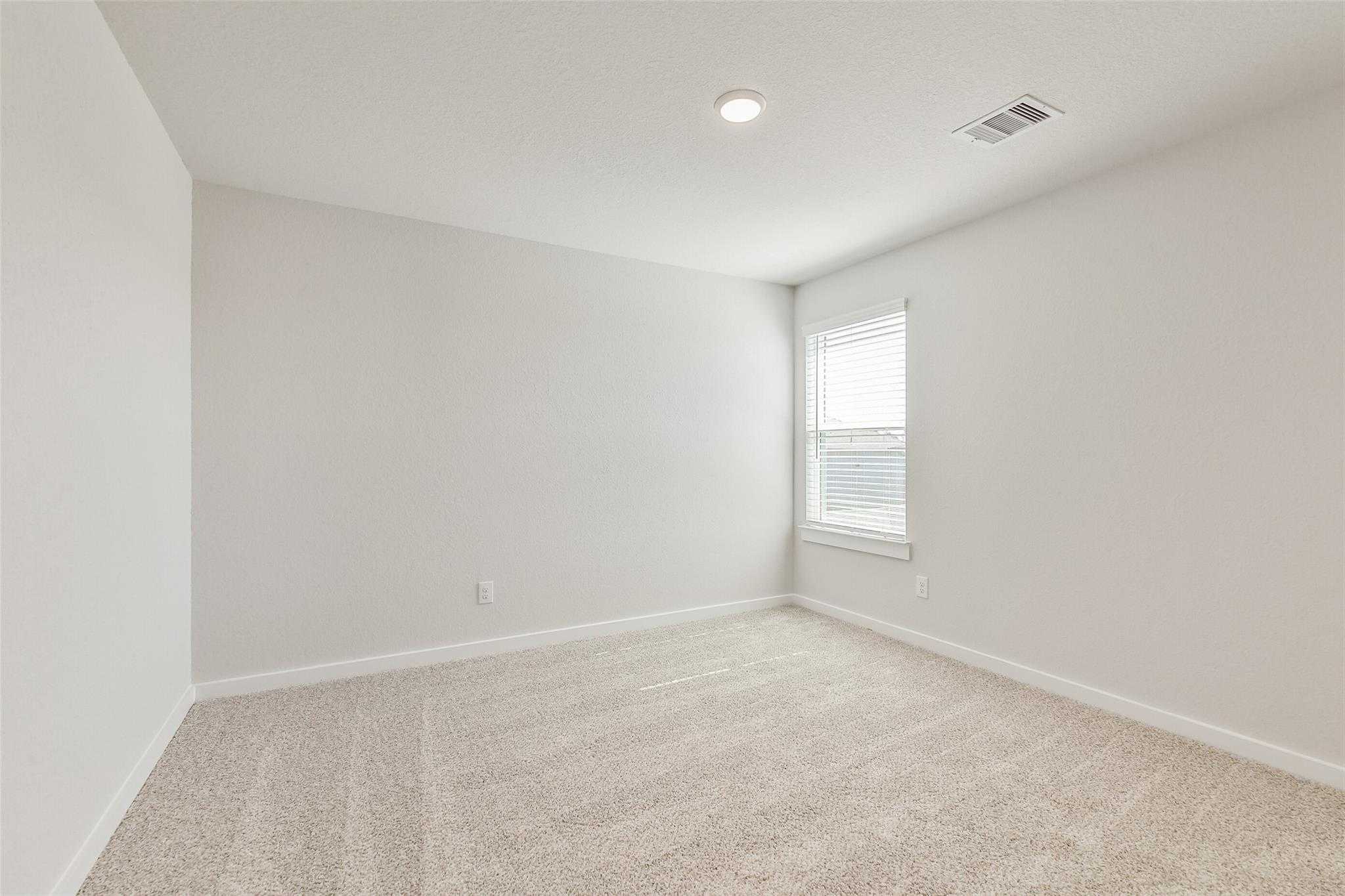 Spacious empty secondary bedroom with neutral walls, beige carpet, and large window in Davidson Homes The Rio Grande H, Magnolia, Texas