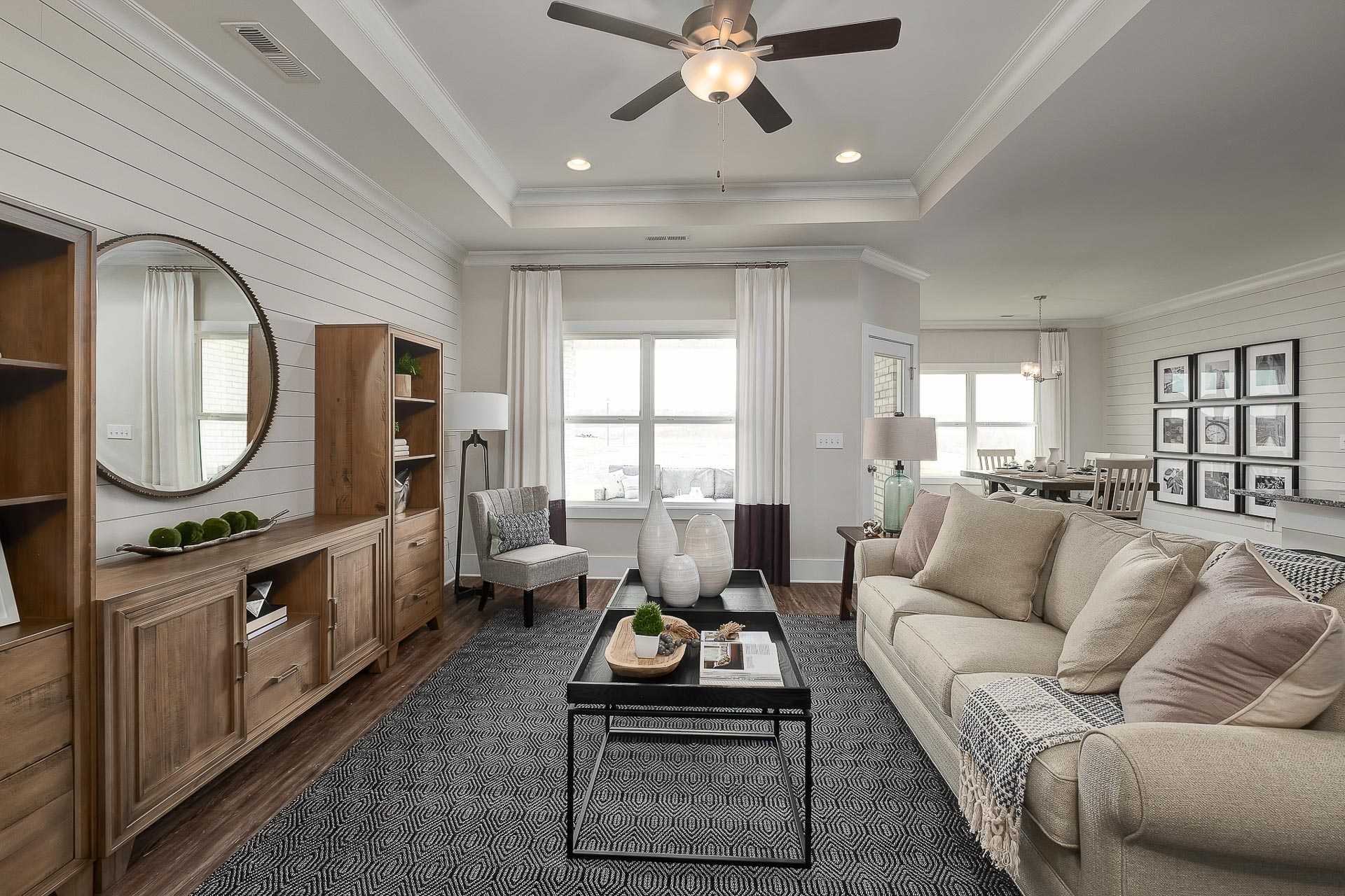 Spacious living room in The Everett C Davidson Homes with shiplap walls, beige sofa, wooden console, ceiling fan, and open dining area
