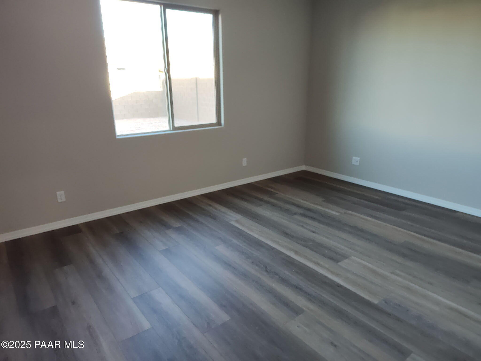 Empty bedroom with gray laminate flooring, neutral walls, and large sunny window in Davidson Homes The Frontier A, Prescott Valley, AZ