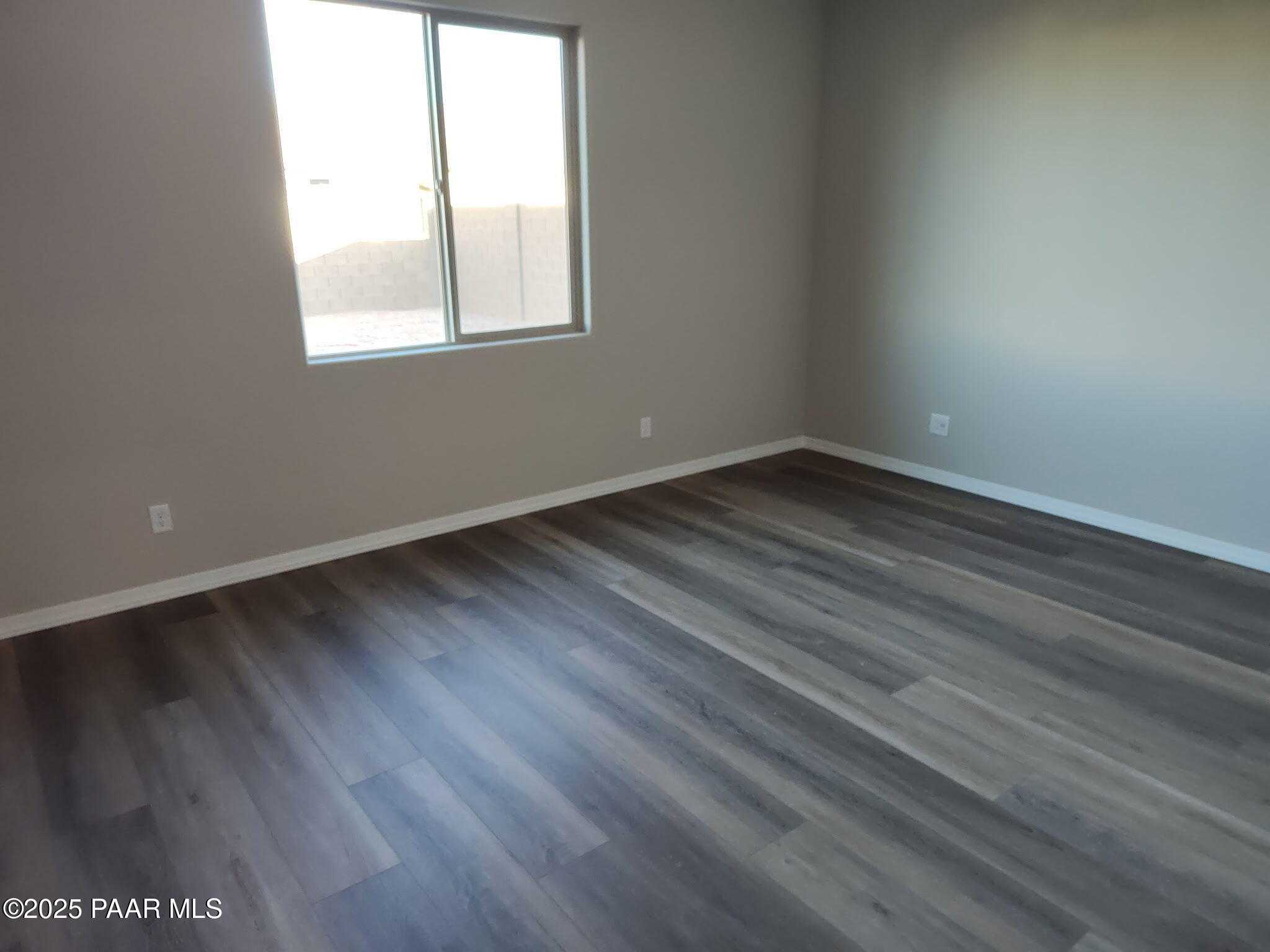 Empty bedroom with gray laminate flooring, neutral walls, and large sunny window in Davidson Homes The Frontier A, Prescott Valley, AZ