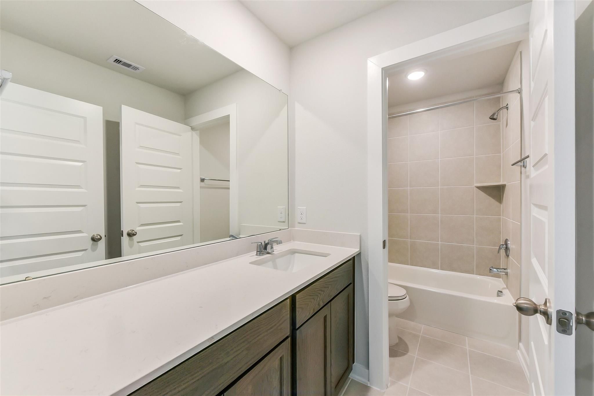 Modern bathroom with quartz vanity, gray cabinets, large mirror, and tub-shower combo in Davidson Homes The Sabine F, Dayton Texas