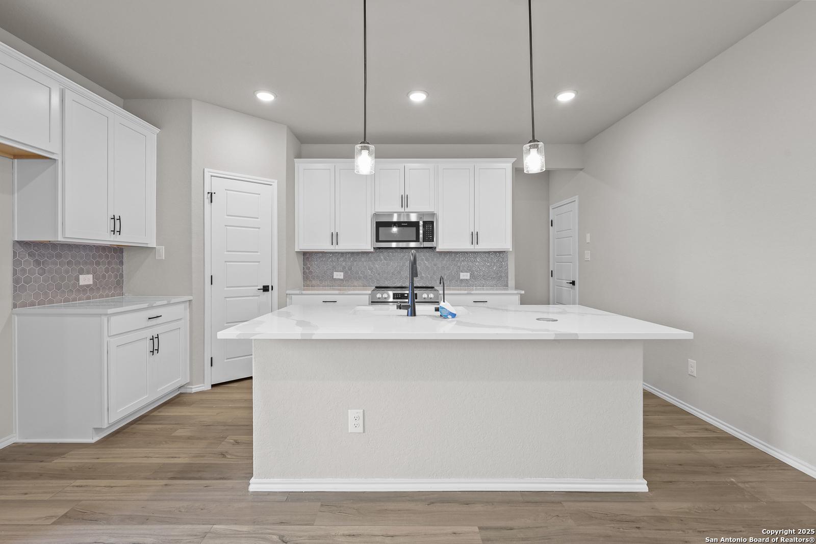 Modern white kitchen island with stainless steel appliances and subway tile backsplash in Davidson Homes The Murray J, San Antonio