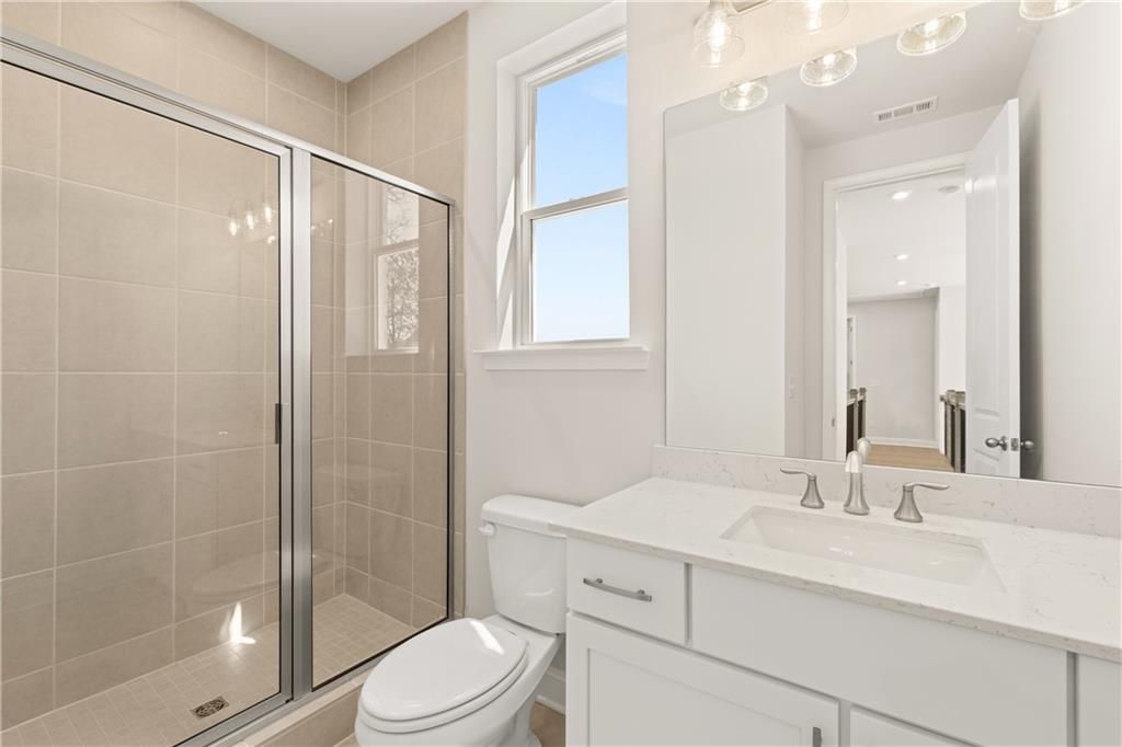 Modern bathroom with glass shower enclosure, beige tile walls, white vanity sink, and window in 5-bedroom Danbury C home, Buford, Georgia
