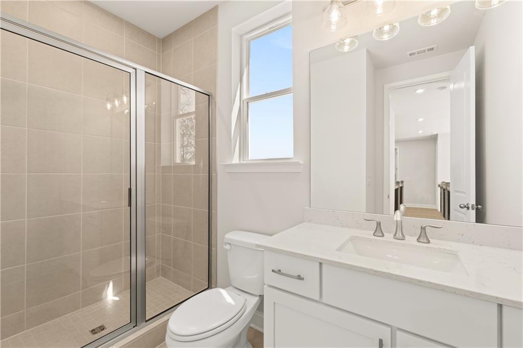 Modern bathroom with glass shower enclosure, beige tile walls, white vanity sink, and window in 5-bedroom Danbury C home, Buford, Georgia