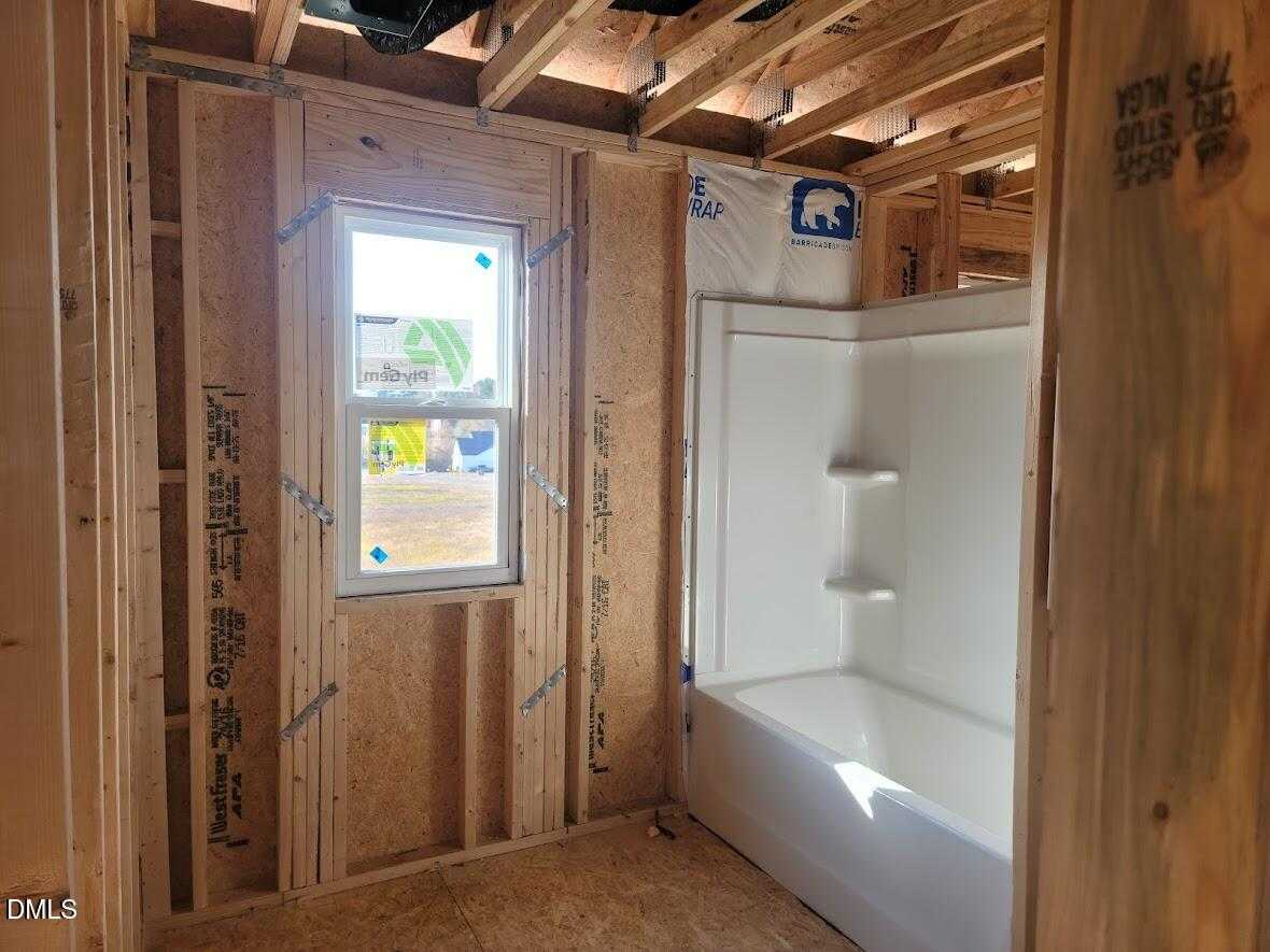 Unfinished bathroom featuring white bathtub and corner shower amid wooden framing in Davidson Homes The Willow G, Angier, NC