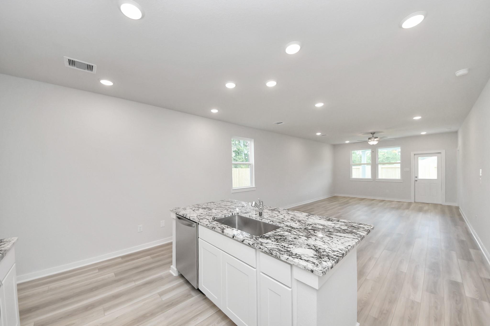 Open-concept kitchen with granite island and light wood floors in The Sabine F floor plan at Liberty Estates, Texas.