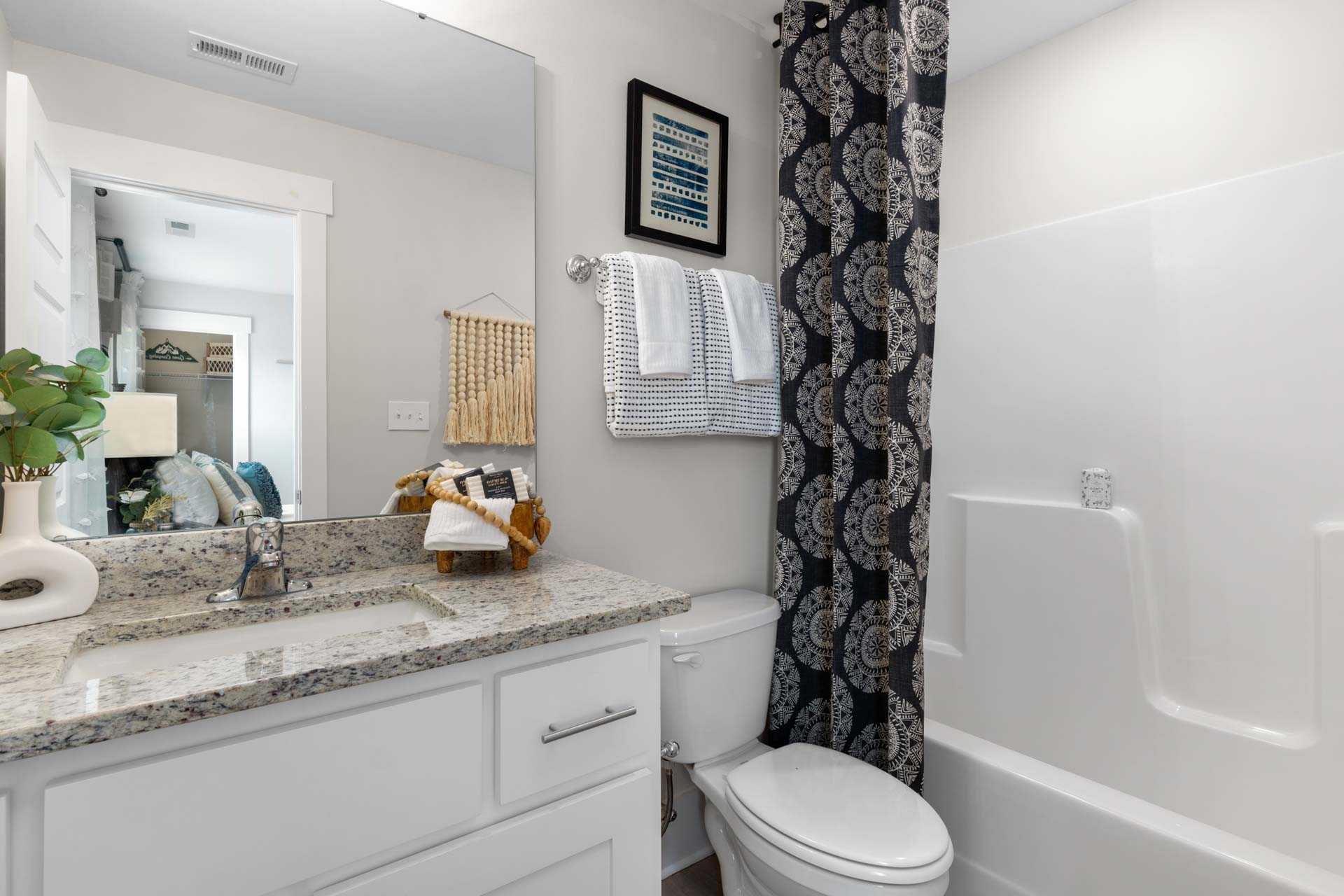 Elegant bathroom at Walker's Hill in Meridianville AL featuring white quartz vanity, large mirror, blue patterned shower curtain, and tub combo
