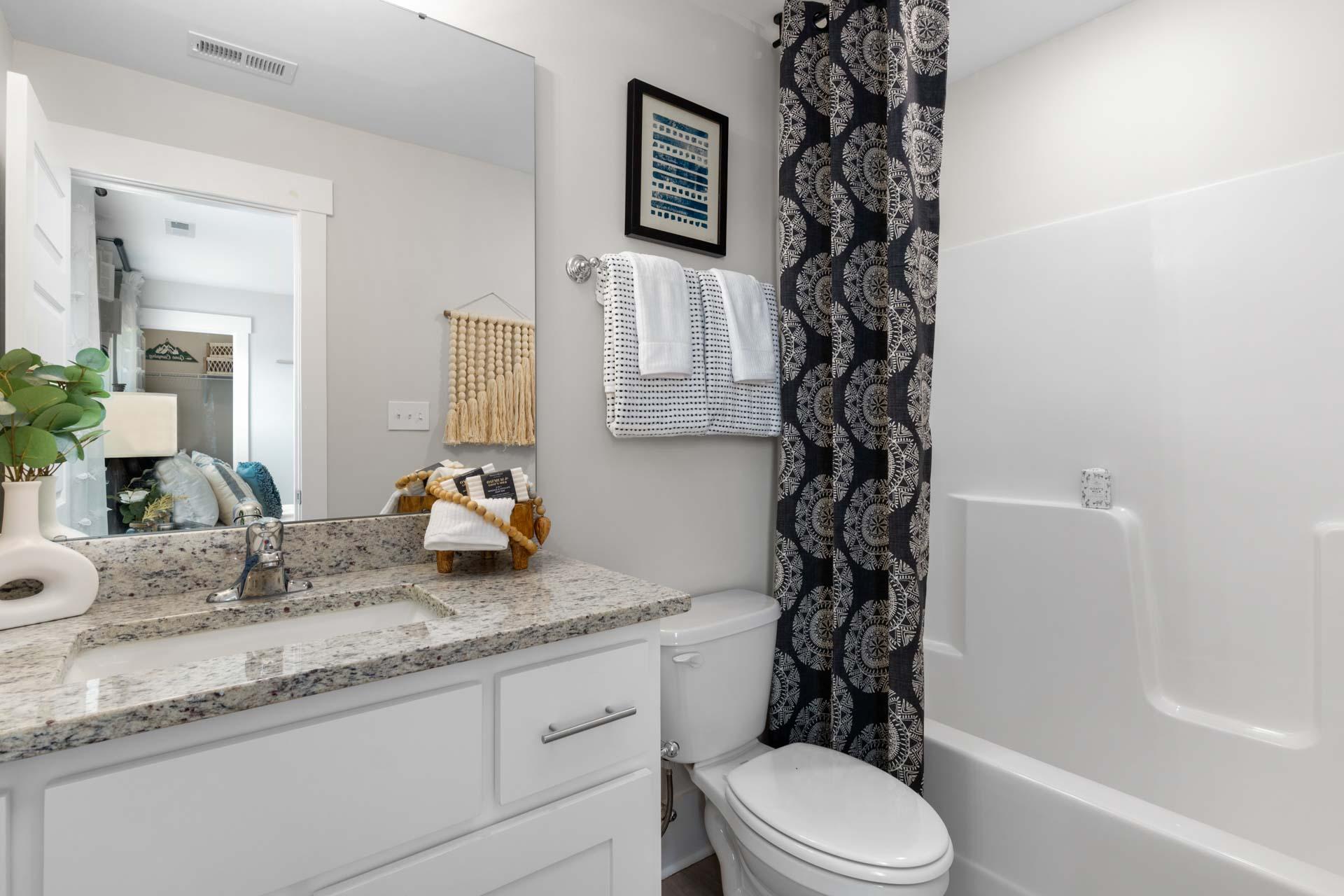 Elegant bathroom at Walker's Hill in Meridianville AL featuring white quartz vanity, large mirror, blue patterned shower curtain, and tub combo