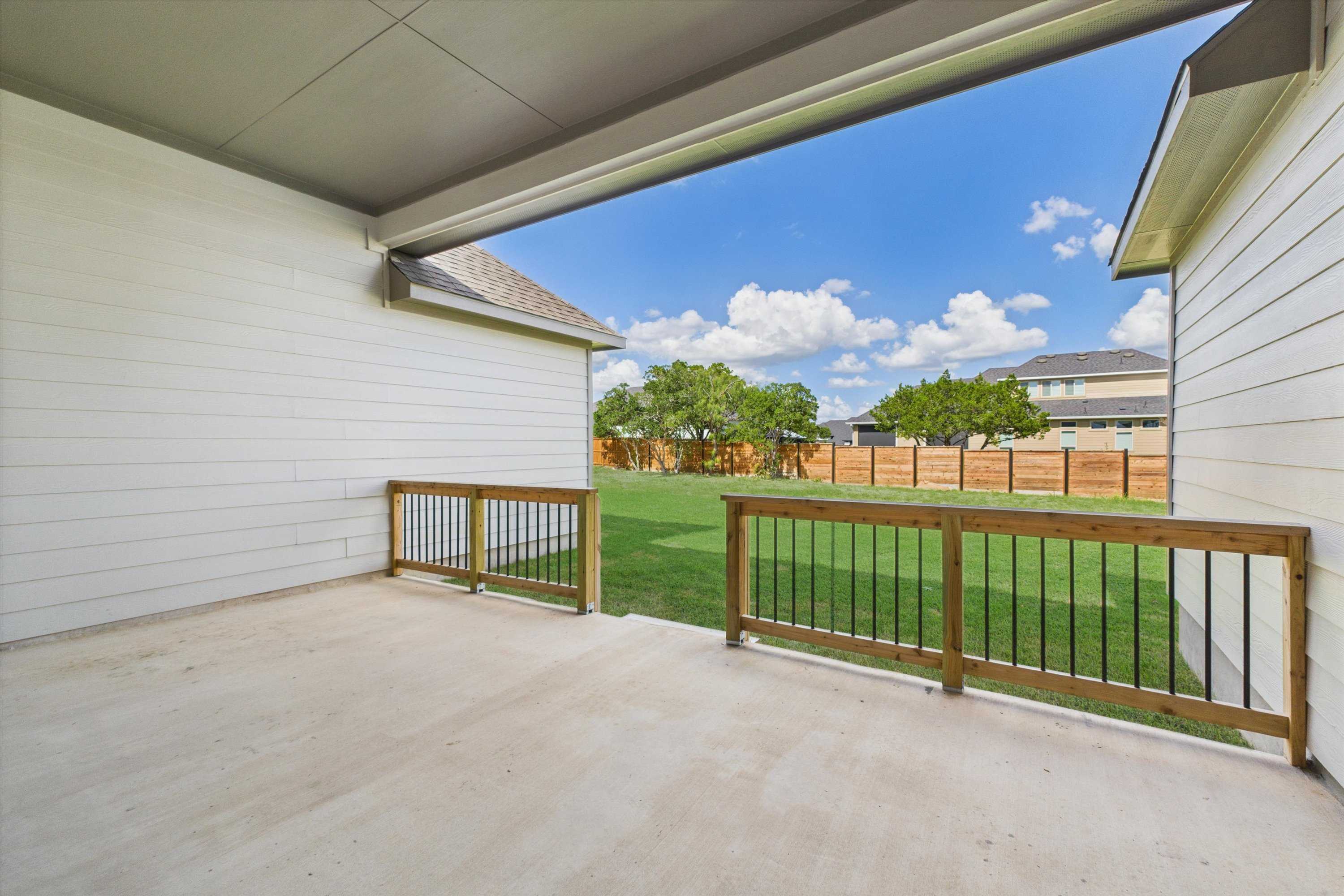 Covered back patio with white siding and wooden railings overlooking green lawn and privacy fence in Davidson Homes The Summerlin C, Castroville, Texas