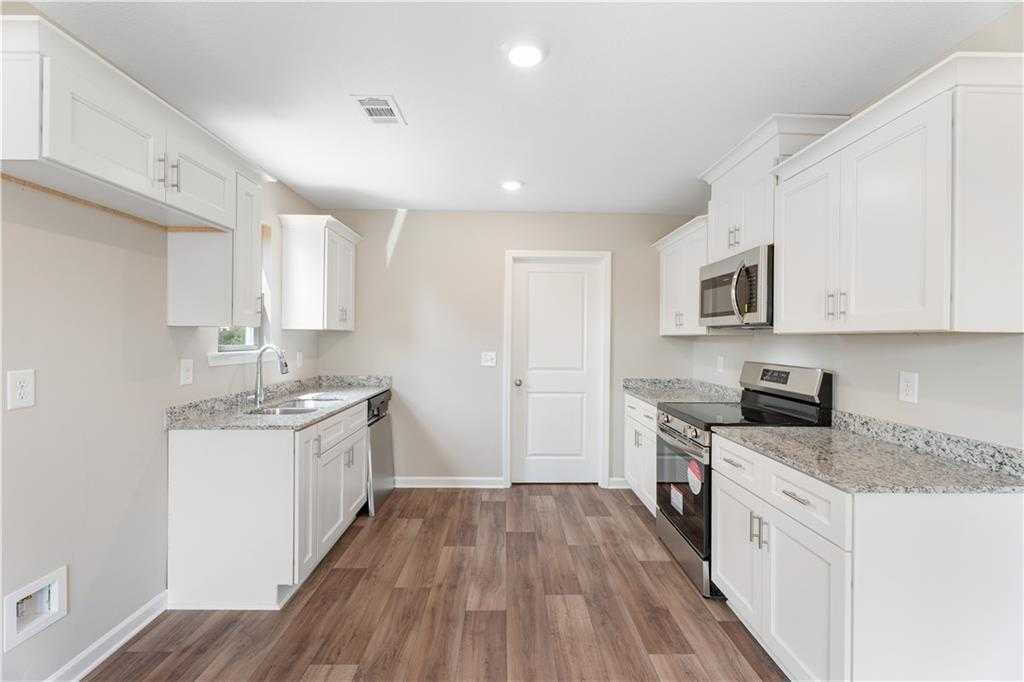 Modern white kitchen with granite countertops, stainless steel appliances, and hardwood floors in Evermore Homes The Washington, Phenix City, AL