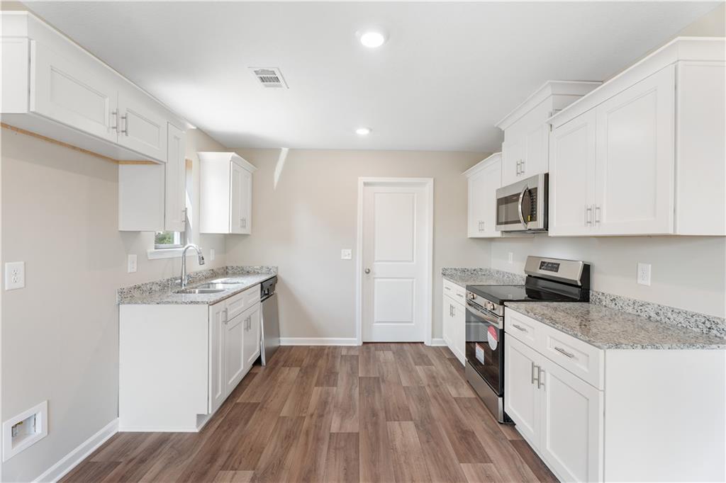 Modern white kitchen with granite countertops, stainless steel appliances, and hardwood floors in Evermore Homes The Washington, Phenix City, AL
