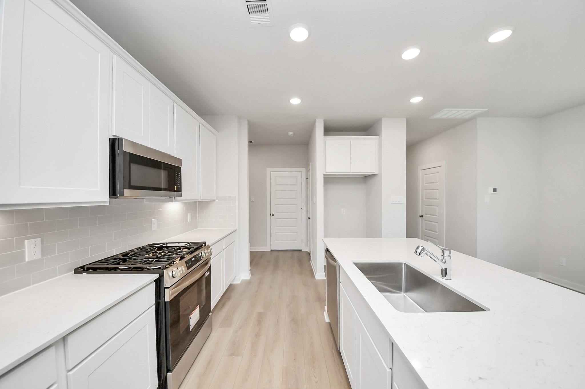 Modern white kitchen with island, stainless appliances, and quartz countertops in The Blanco E floor plan, Conroe, Texas.