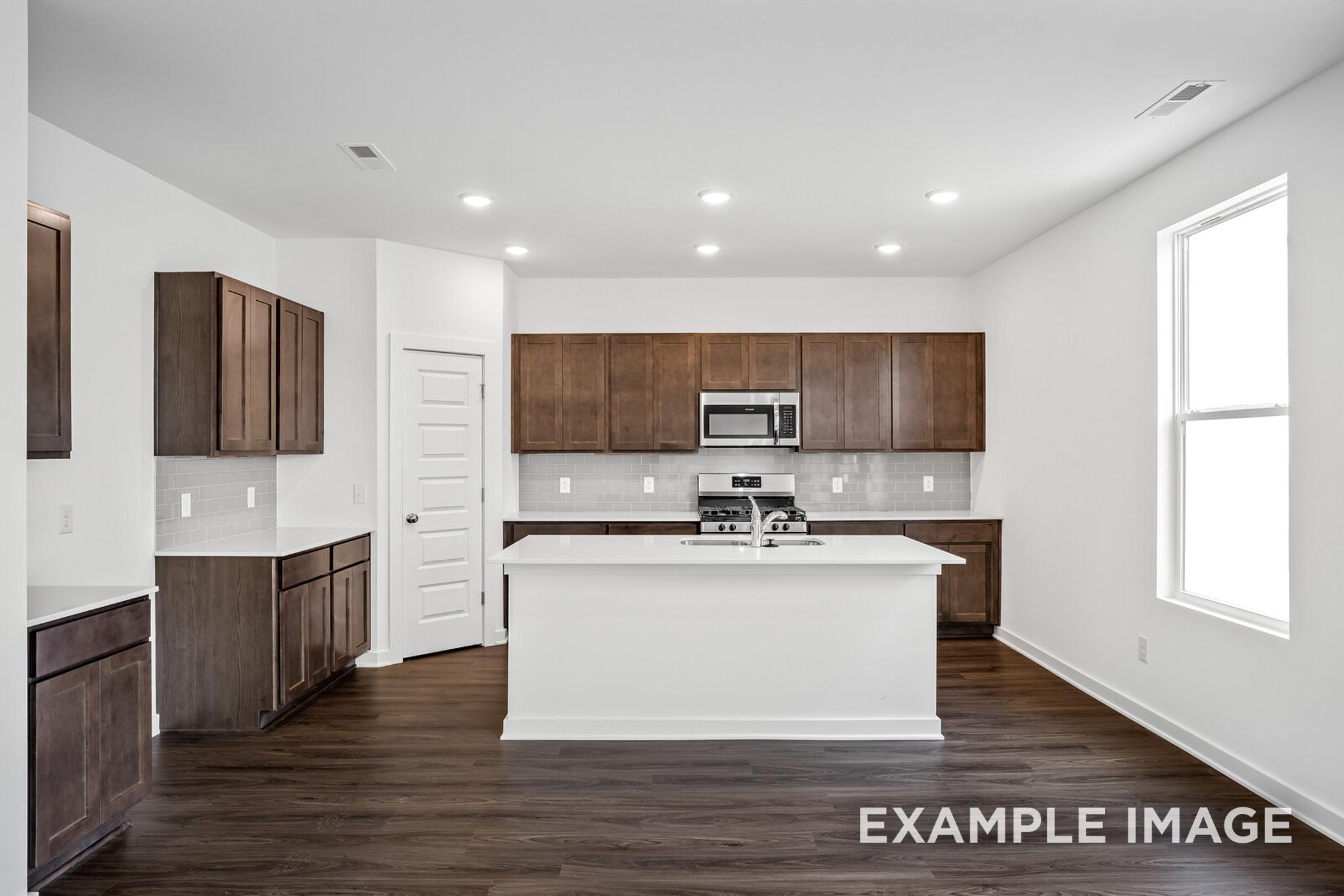 Spacious modern kitchen in The Logan C with white island, shaker cabinets, stainless steel appliances, and large window