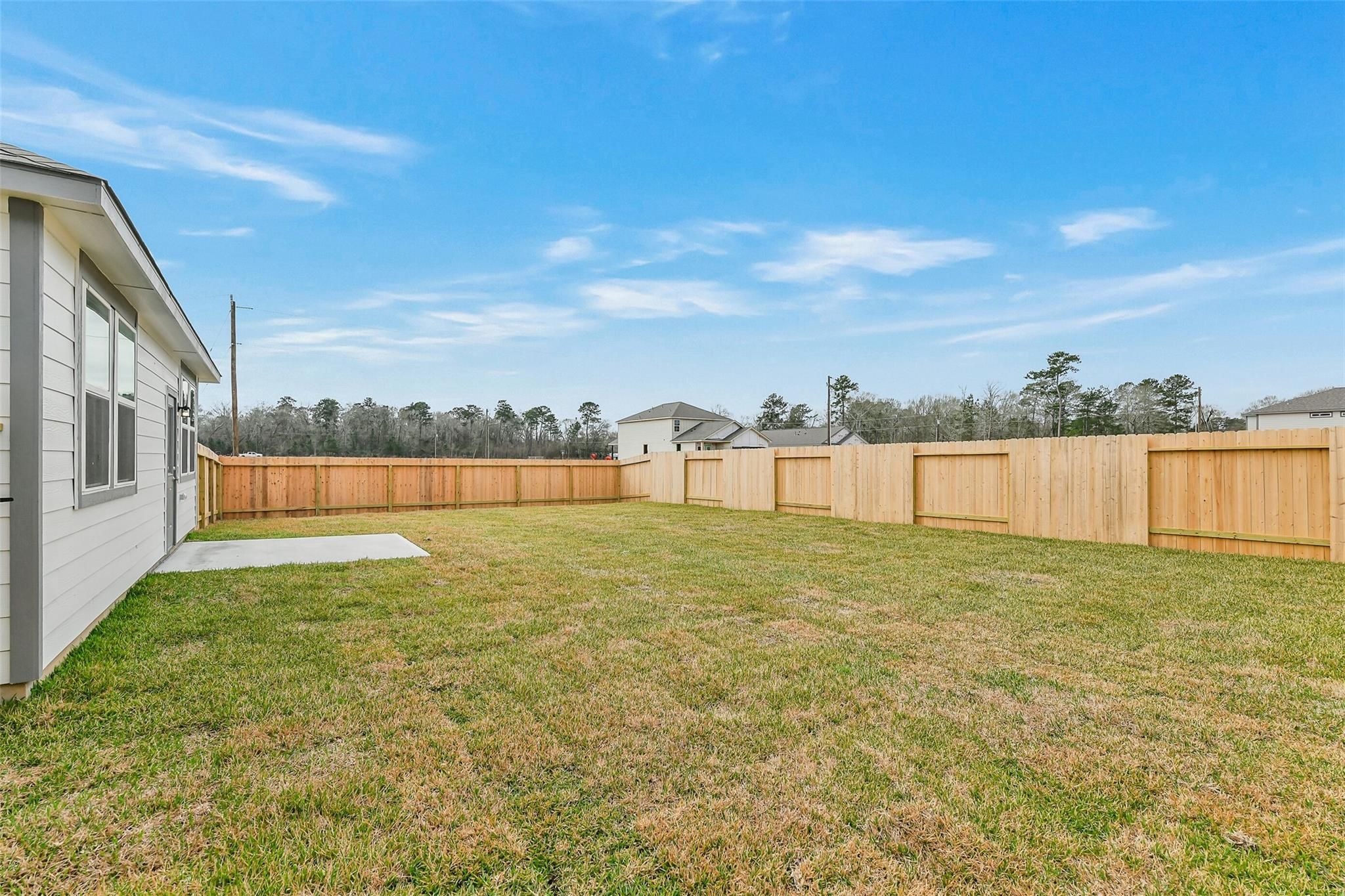 Spacious grassy backyard with wooden privacy fence and blue sky in 5-bedroom The Brazos E home, Liberty Estates, Cleveland, Texas